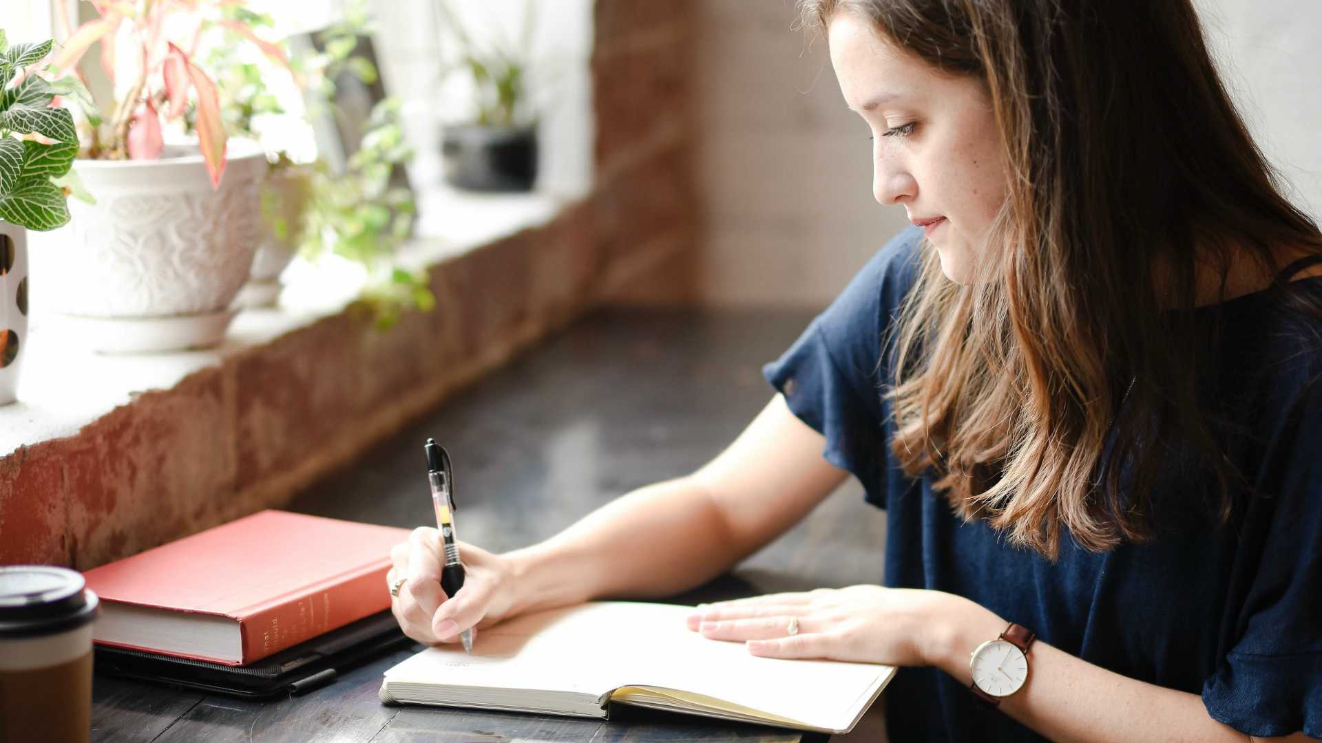 woman writing in a journal next to a window