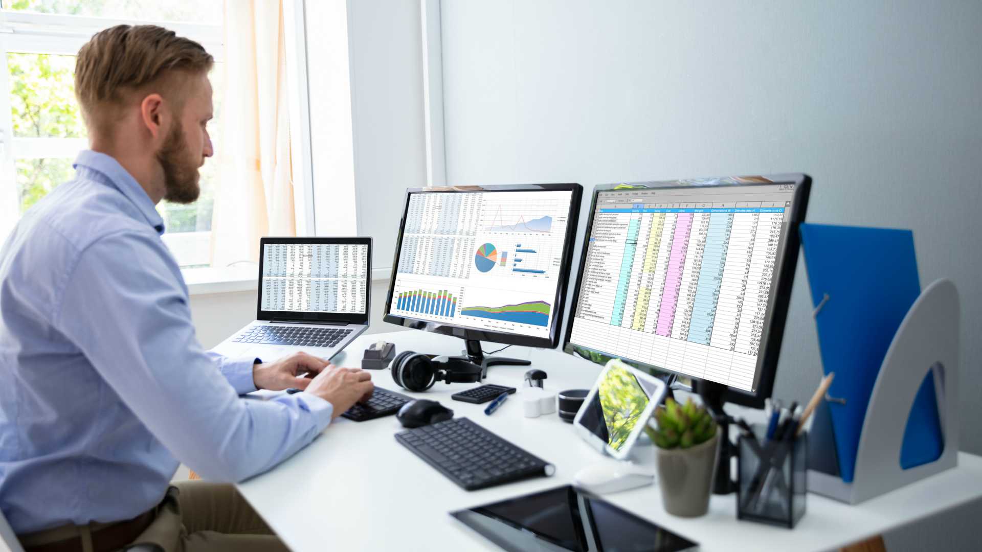 Young businessman working at office setup with three desktop monitors, analyzing data