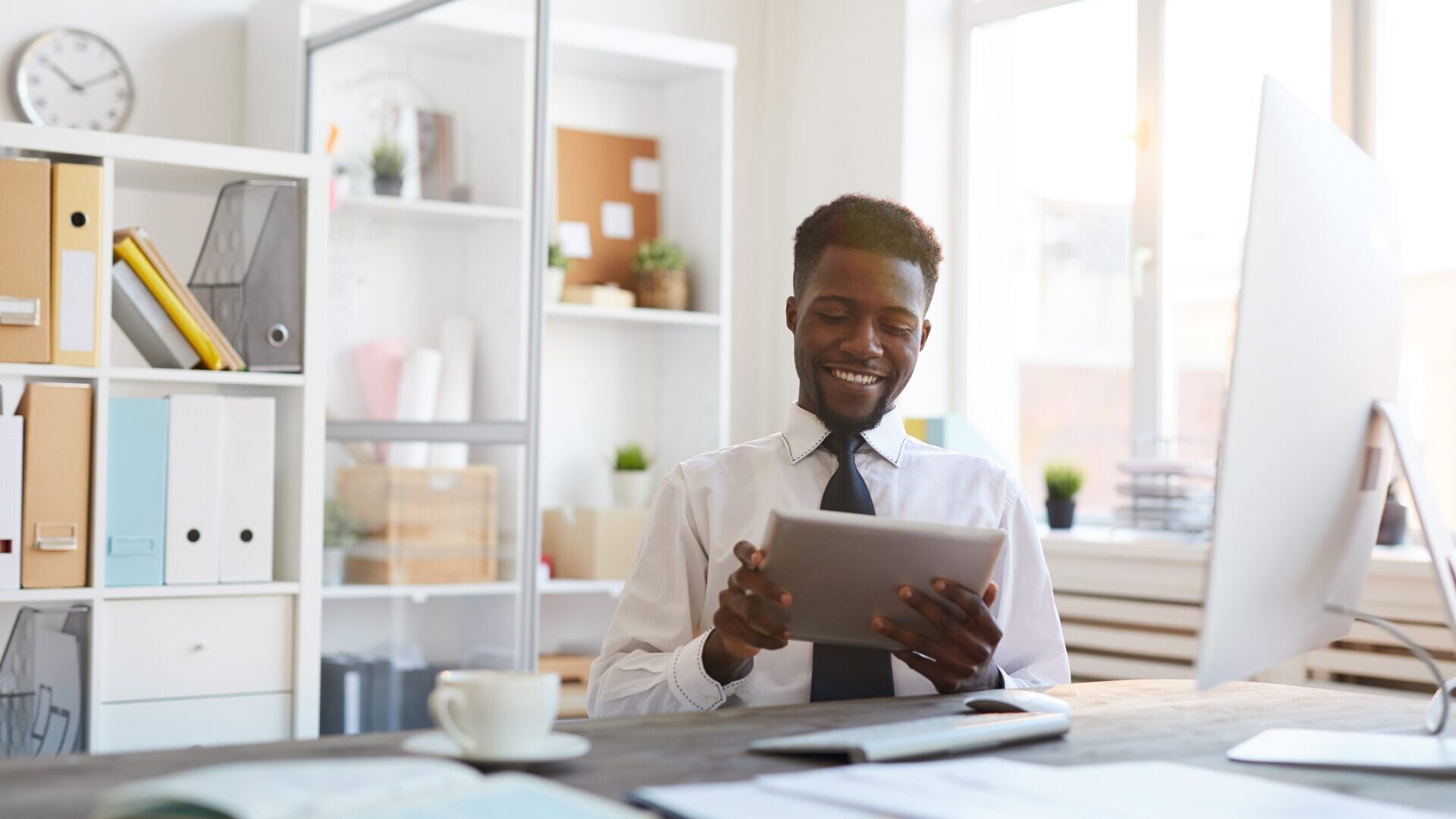 Young smiling African-american broker with tablet looking through online rates on brokerage websites