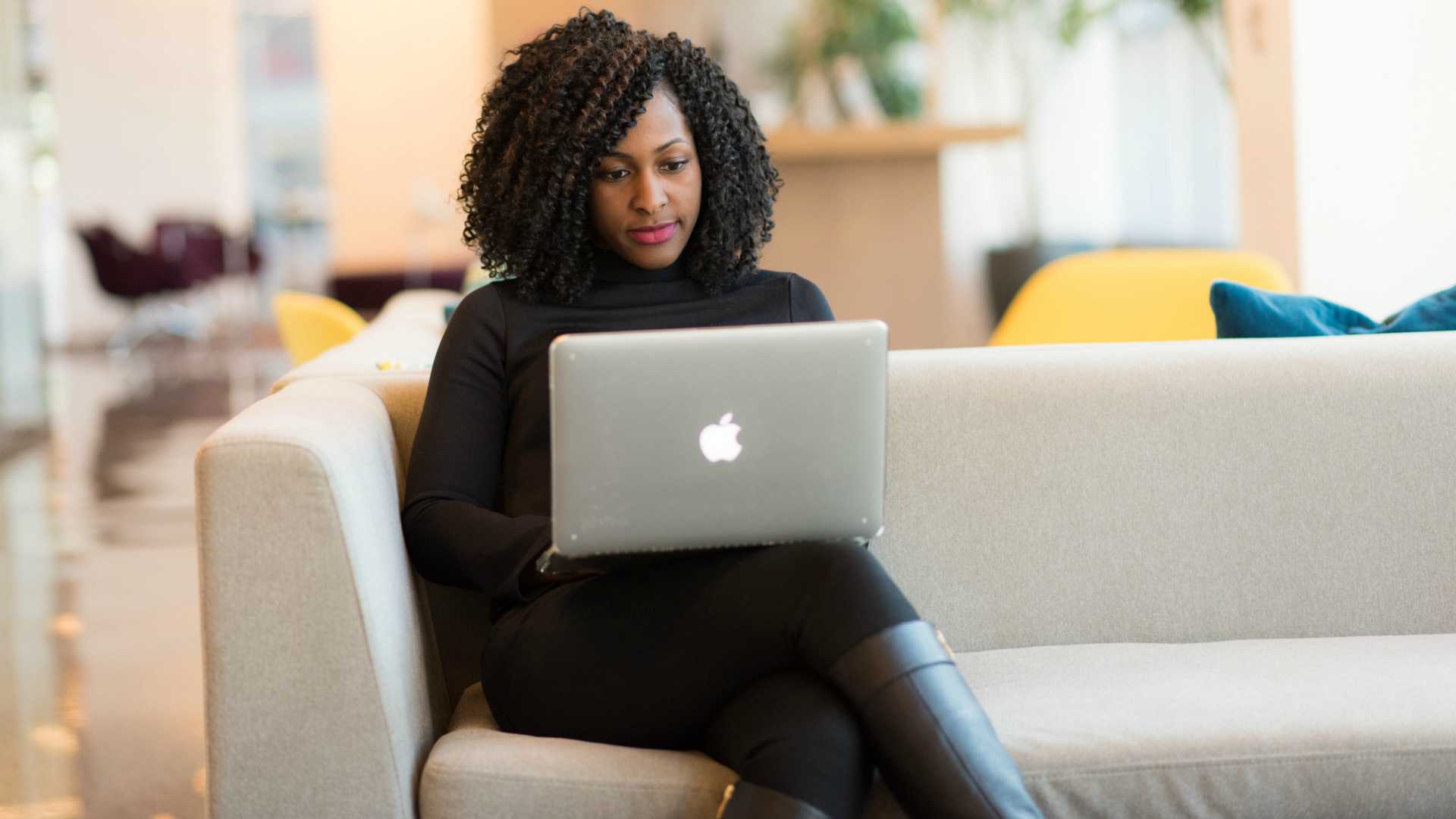Young businesswoman sitting on couch in trendy workspace and working on laptop