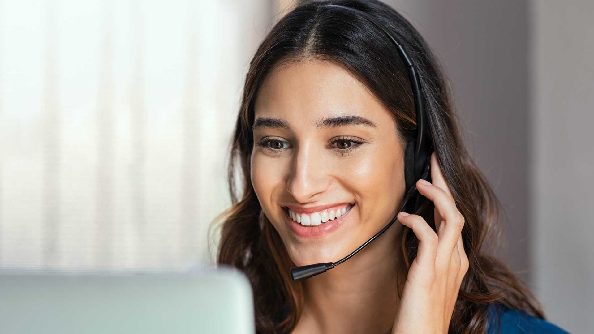 Smiling woman using laptop while talking to customer on phone.