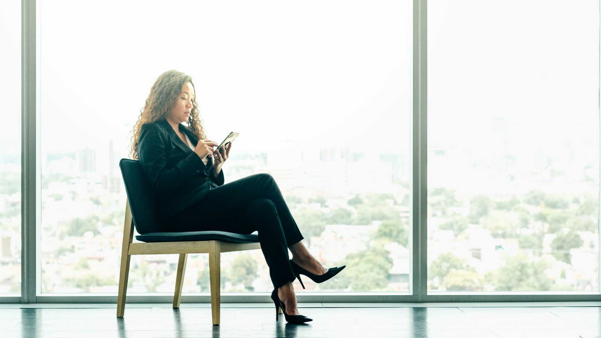 Businesswoman participating in learning on smartphone in front of a large window
