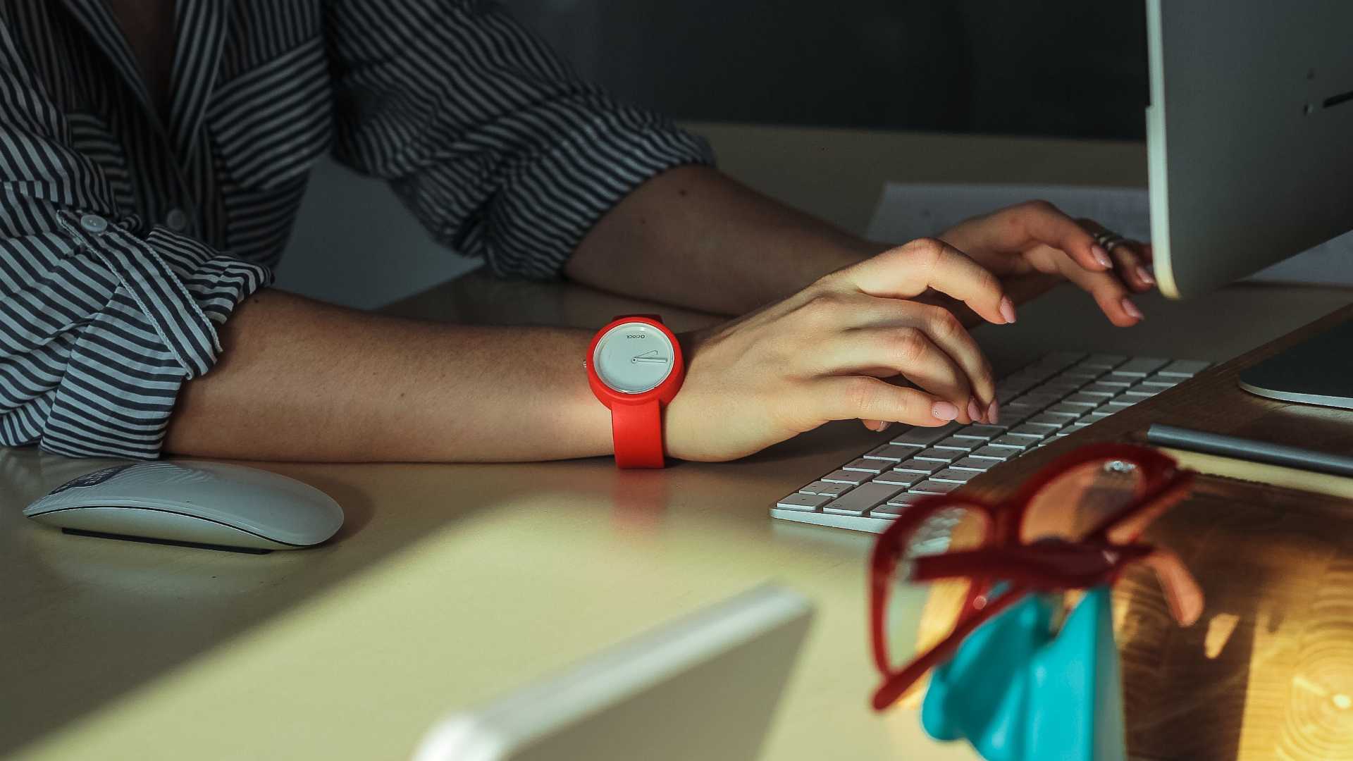 Businessperson wearing red watch working at desk on desktop computer
