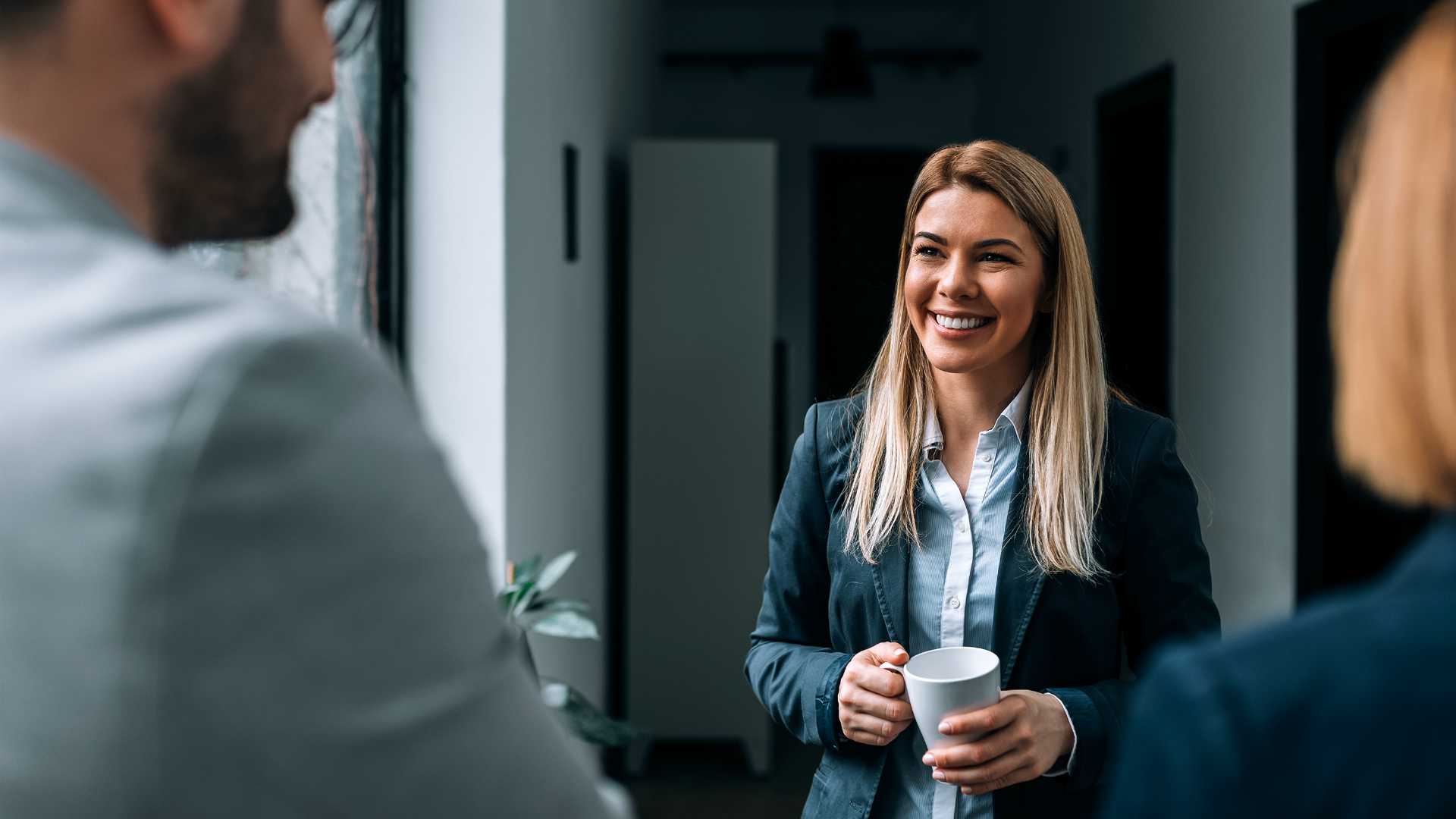 Smiling businesswoman drinking a cup of coffee with her colleagues.
