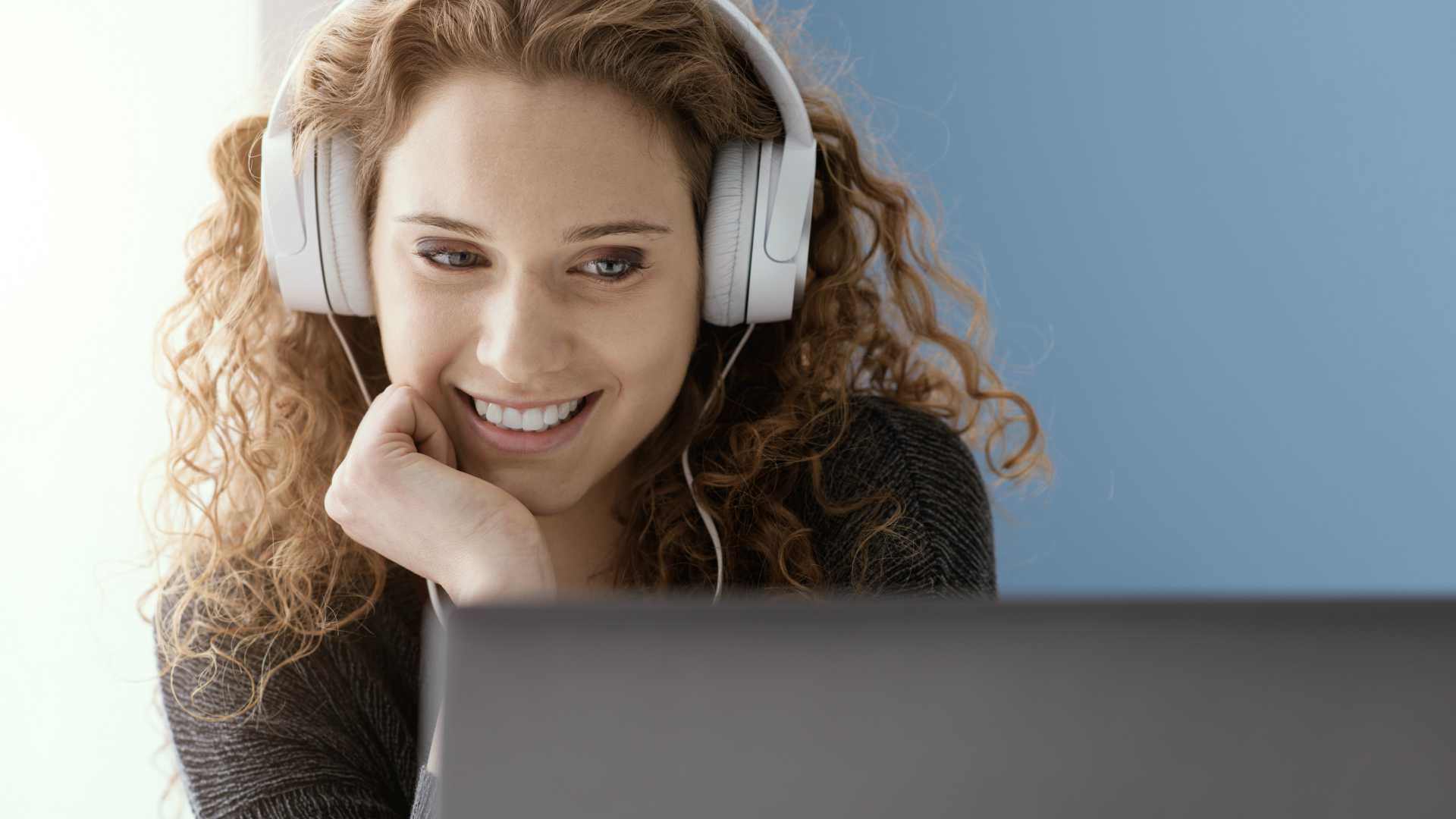 Young smiling girl wearing headphones and watching films online on her laptop