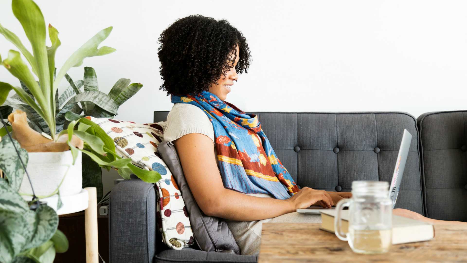 Remote female worker sitting on couch in apartment and working on laptop