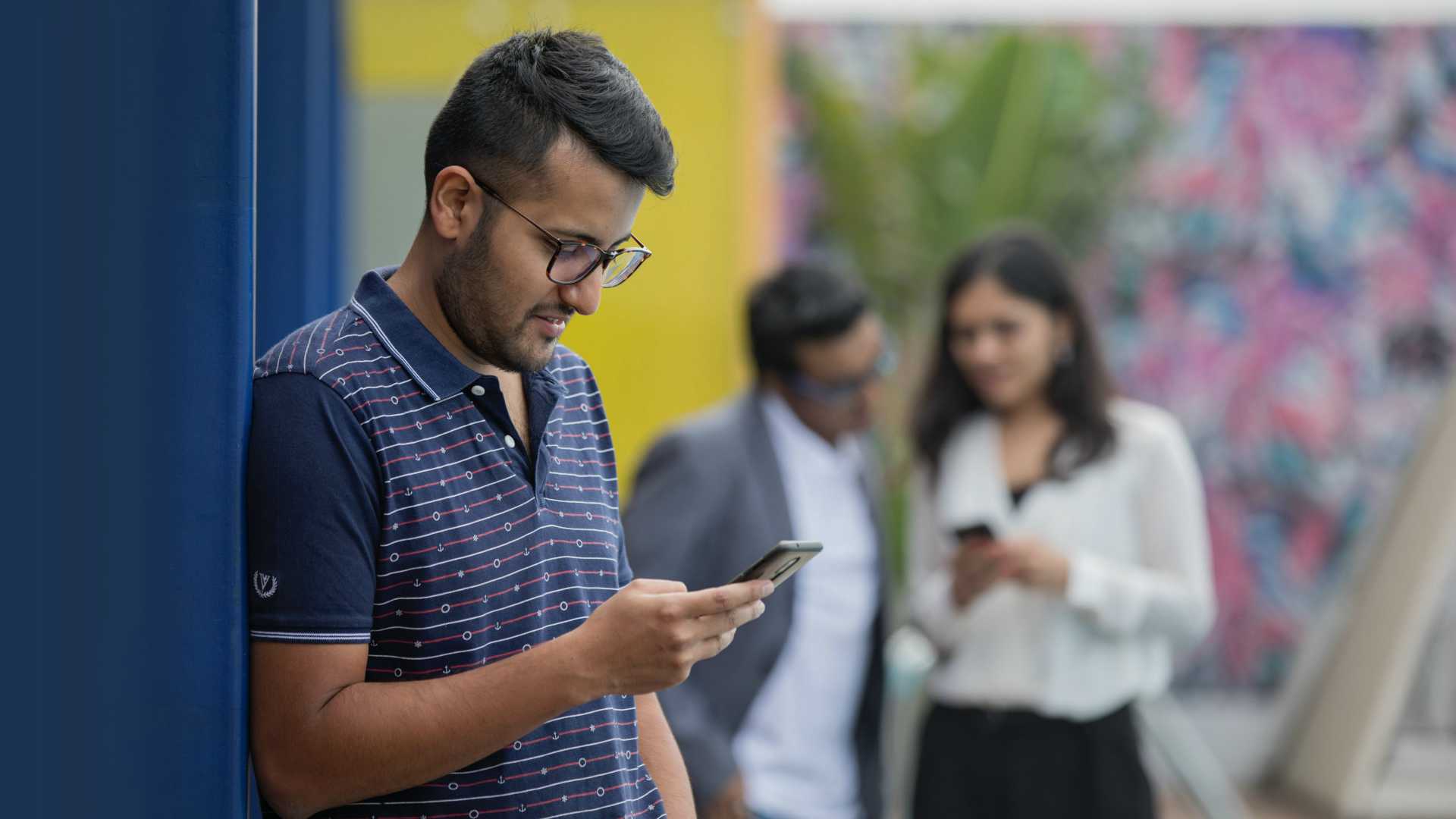 Businessman on phone with two other colleagues looking at phone in background, engaging in mobile learning