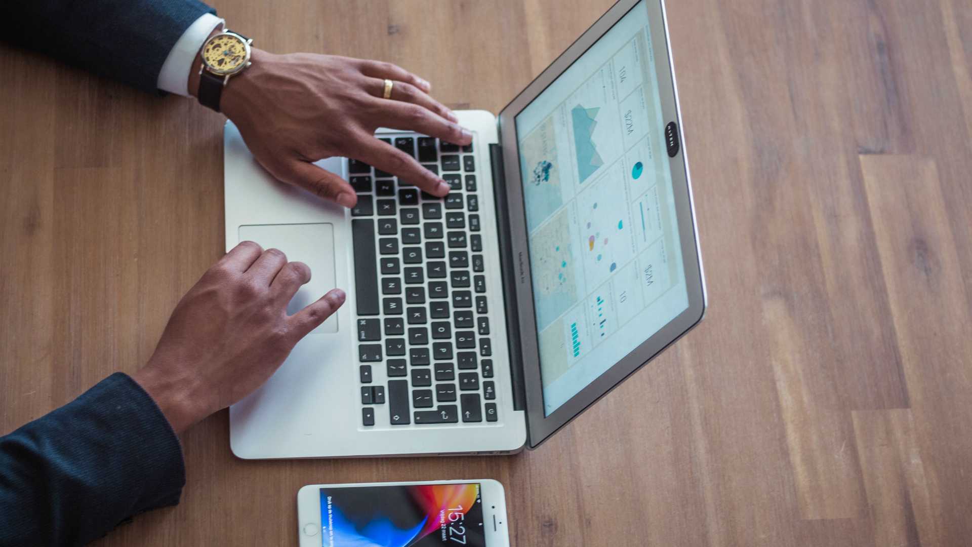 man's hands typing on a laptop with charts on it