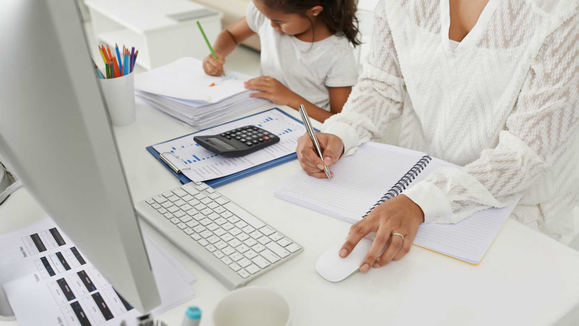 Business woman making notes in textbook, her daughter sitting next to her and drawing