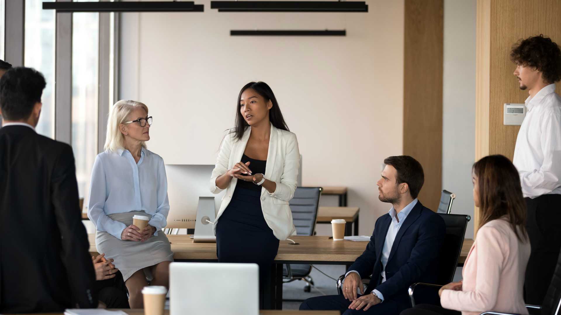 Serious young businesswoman speaking at diverse corporate group meeting
