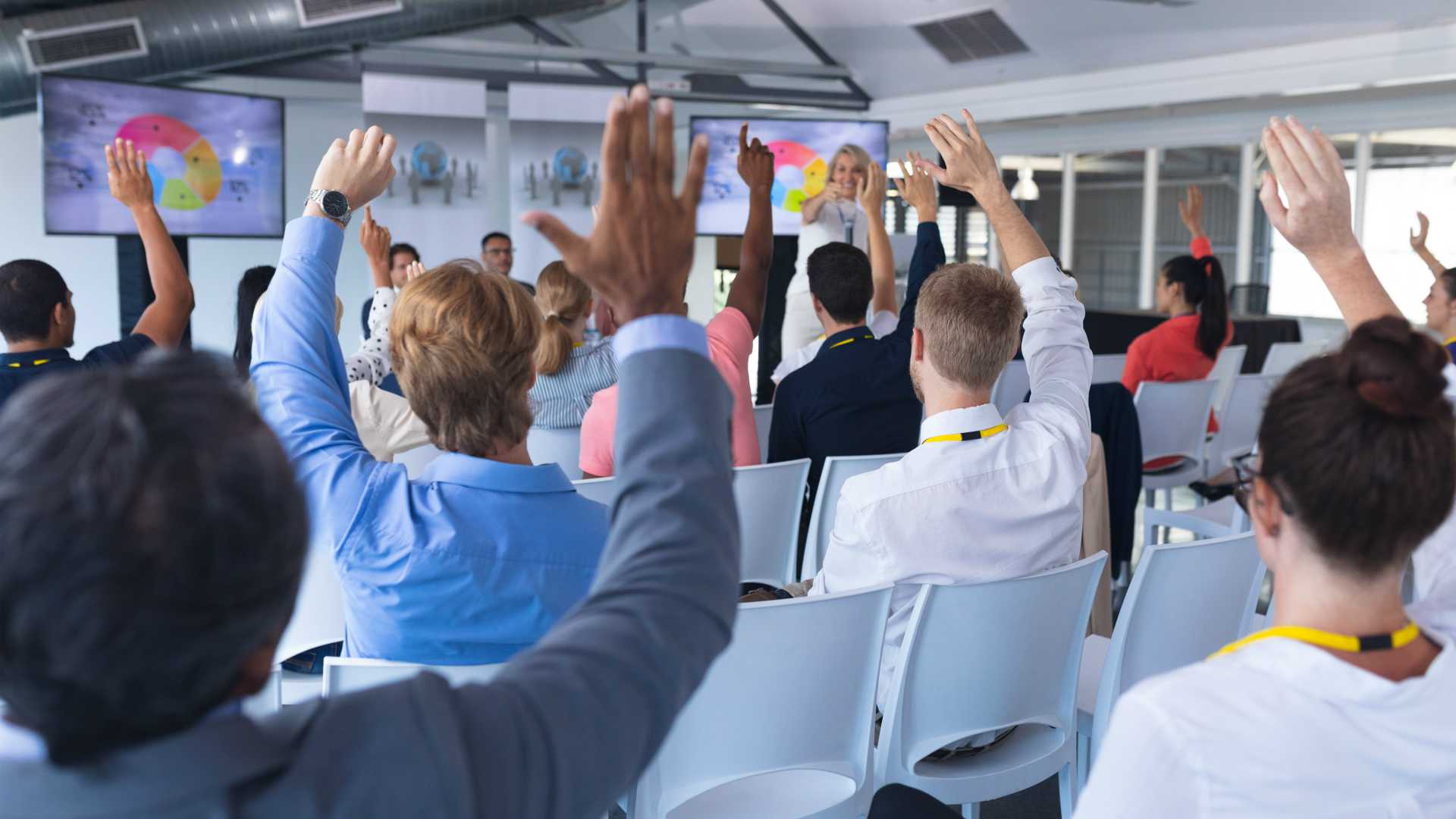 View from the back of classroom of room full of students raising their hands