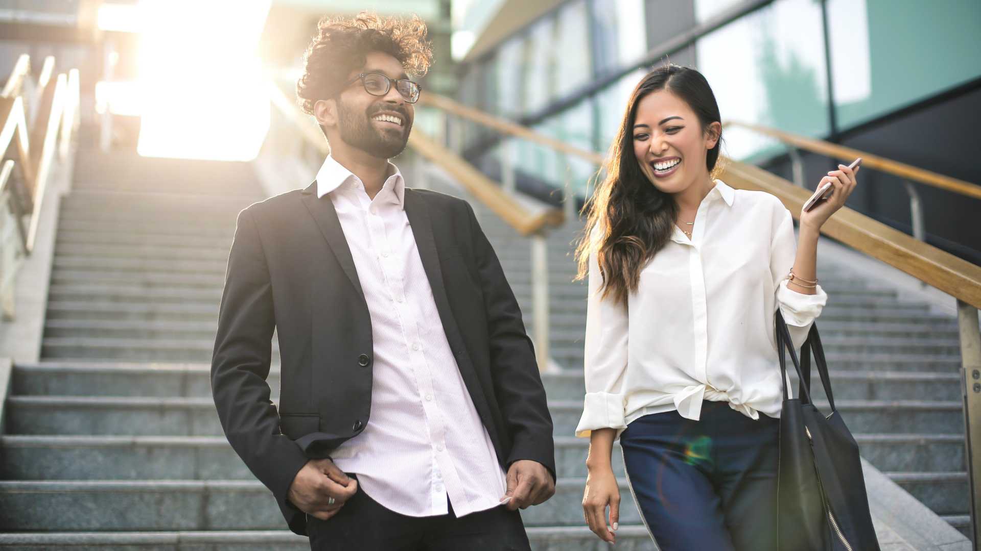Boss and employee laughing and walking down the stairs with sun shining down behind them