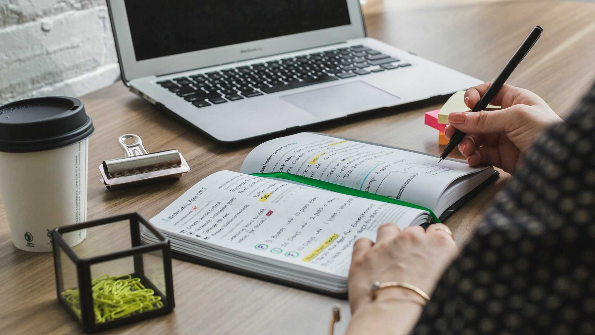 Business manager jotting down notes in notebook in front of computer