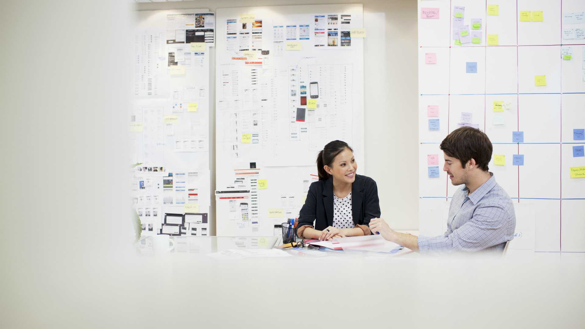 Businessman and businesswoman discussing performance improvement in white, well lit office space