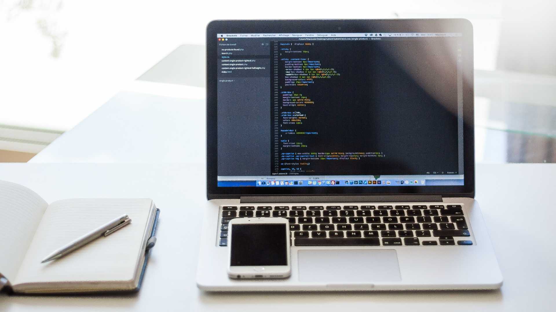Open notebook, laptop, and smart phone sitting on tidy, well lit white desk