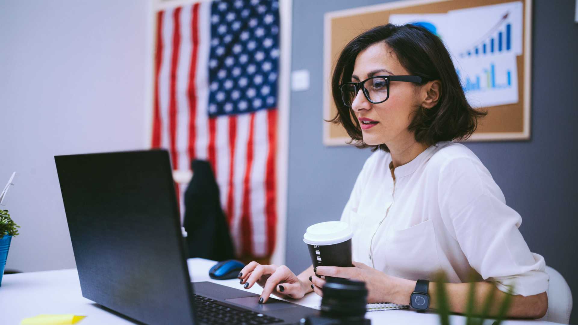 woman working on a laptop with an American flag hanging on the wall
