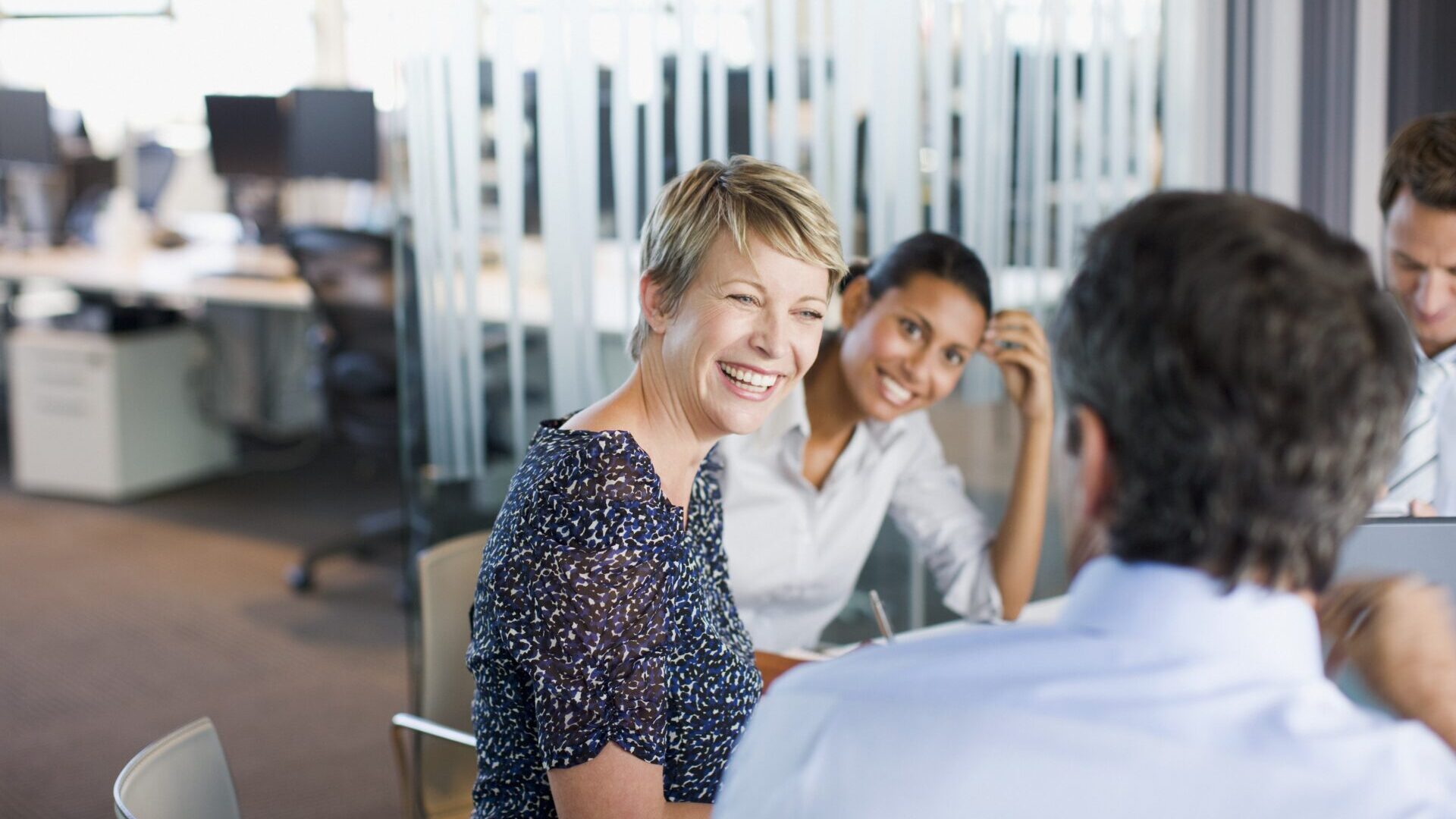 Businesswoman laughing and collaborating with teammates around conference room table