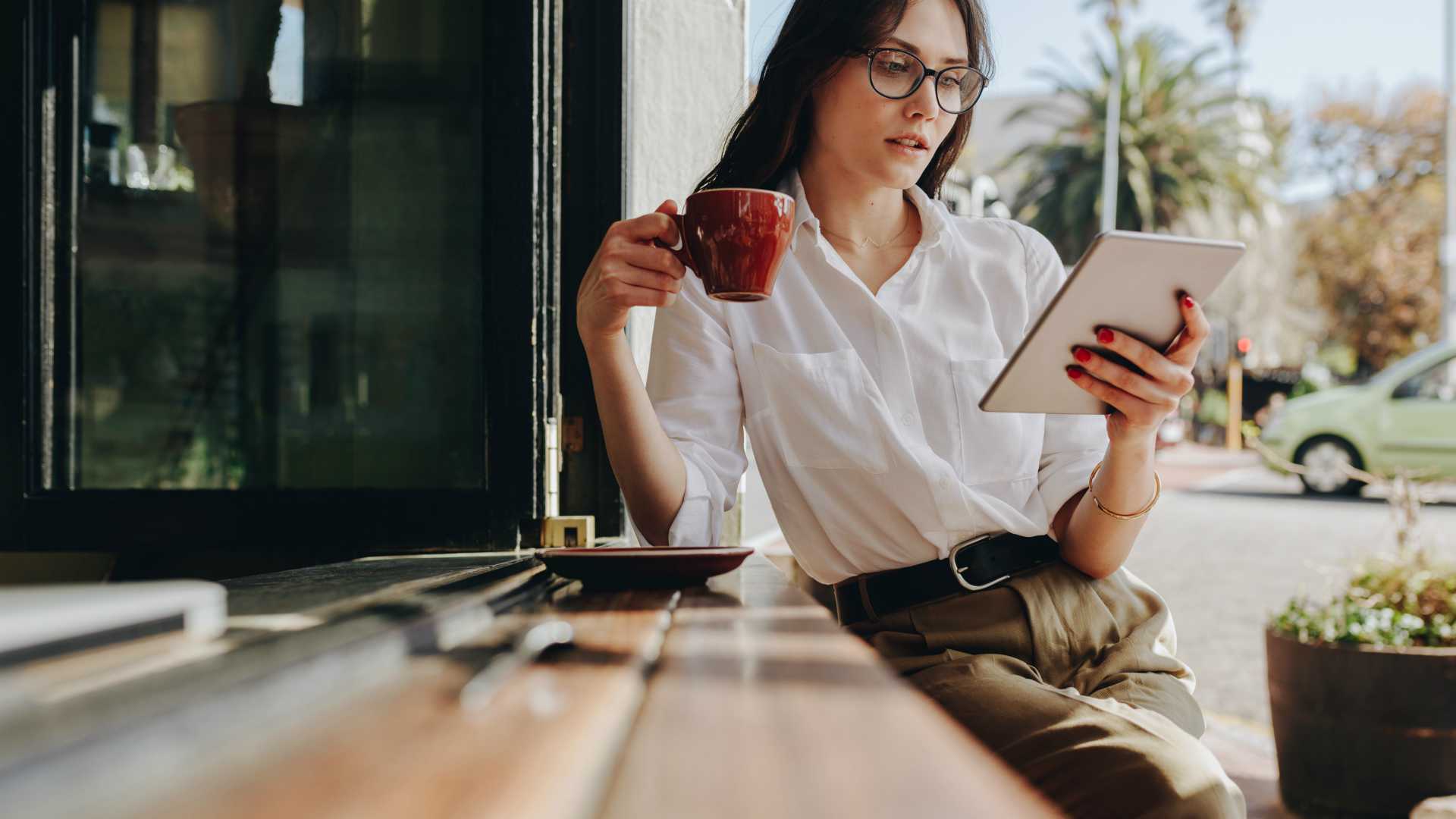 Female entrepreneur relaxing at coffee shop having coffee and reading email on her digital tablet.