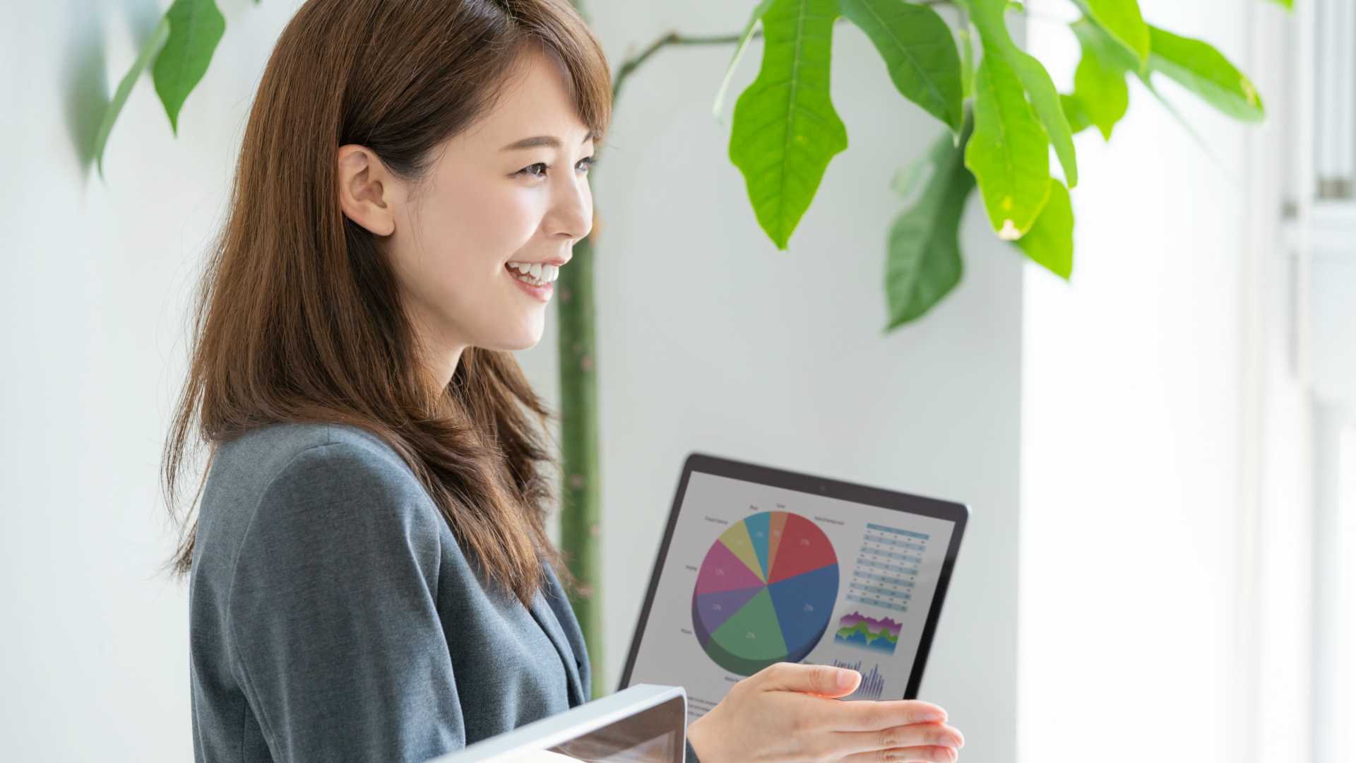 Young woman presenting with laptop in background displaying pie chart