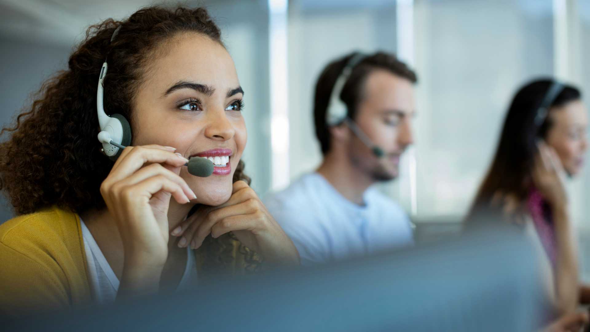 Smiling young service professional chatting in headset to customer on the other line