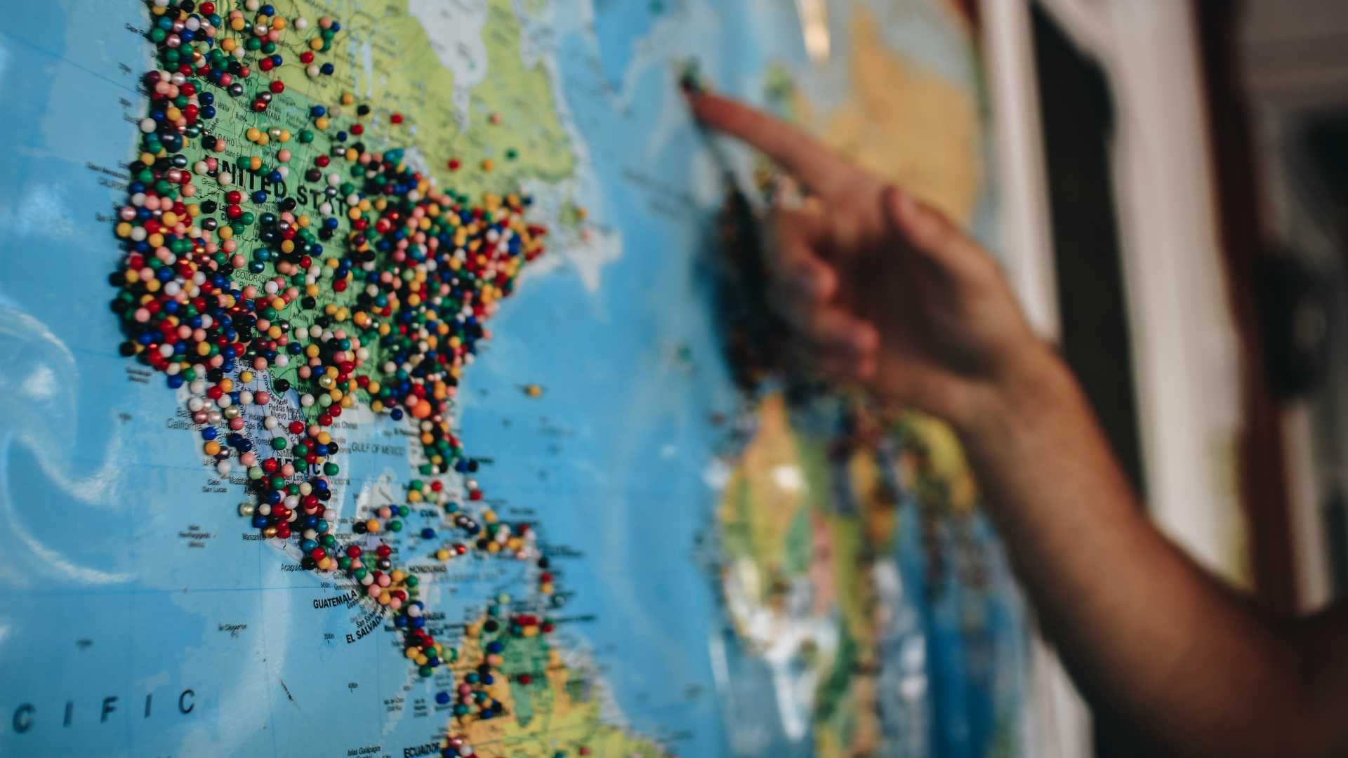 Businessperson pointing to spot on a map of the globe covered in pins