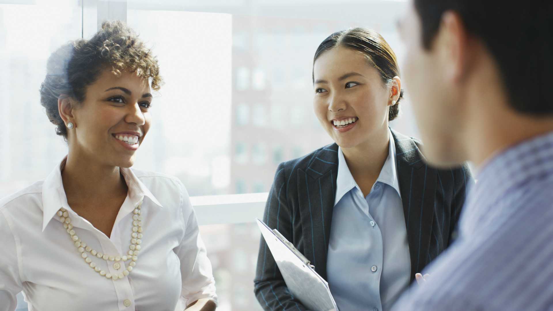 Three colleagues smiling and chatting among one another in a brightly lit, modern office