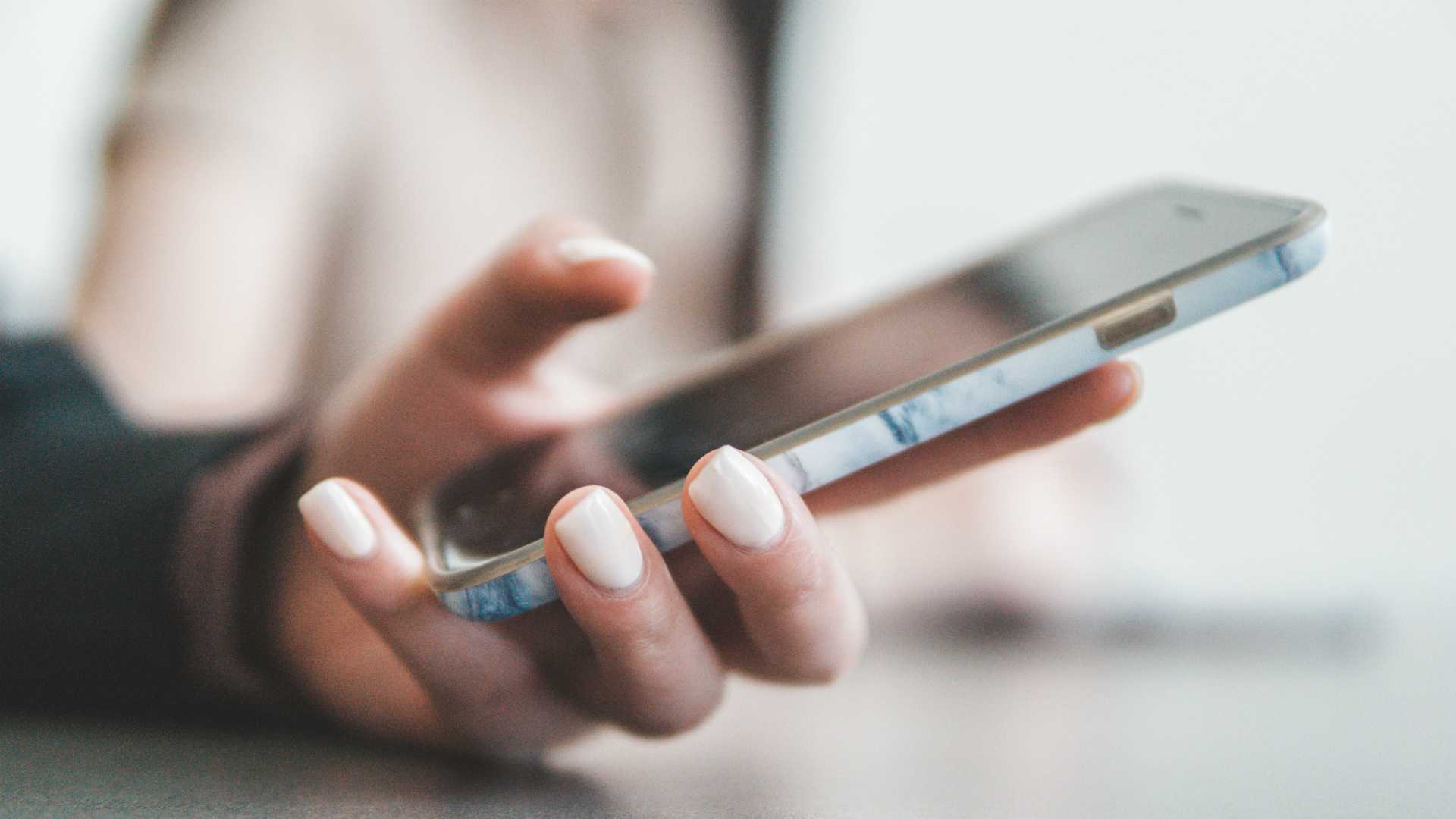 Frontline worker with painted nails holding cell phone and engaging in learning