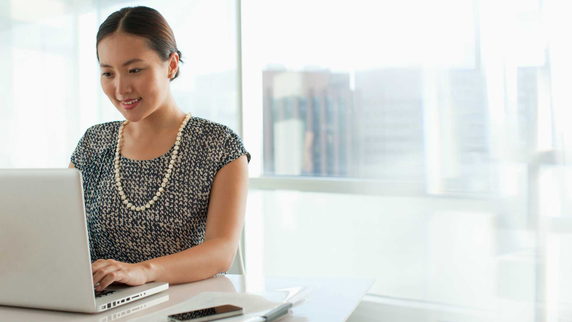 Young woman sitting at desk in brightly lit room participating in a customer education program on laptop