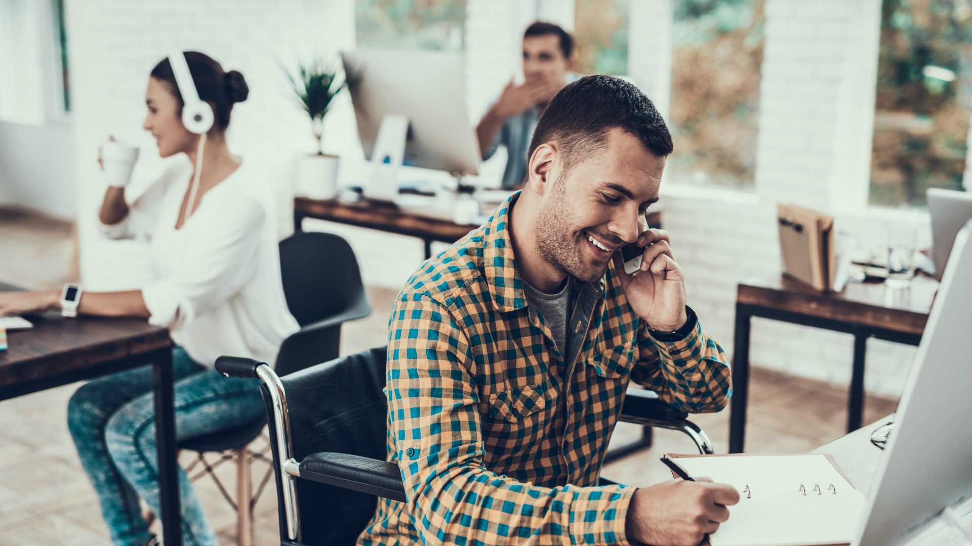 Young businessman chatting on phone and jotting down notes while sitting at desk