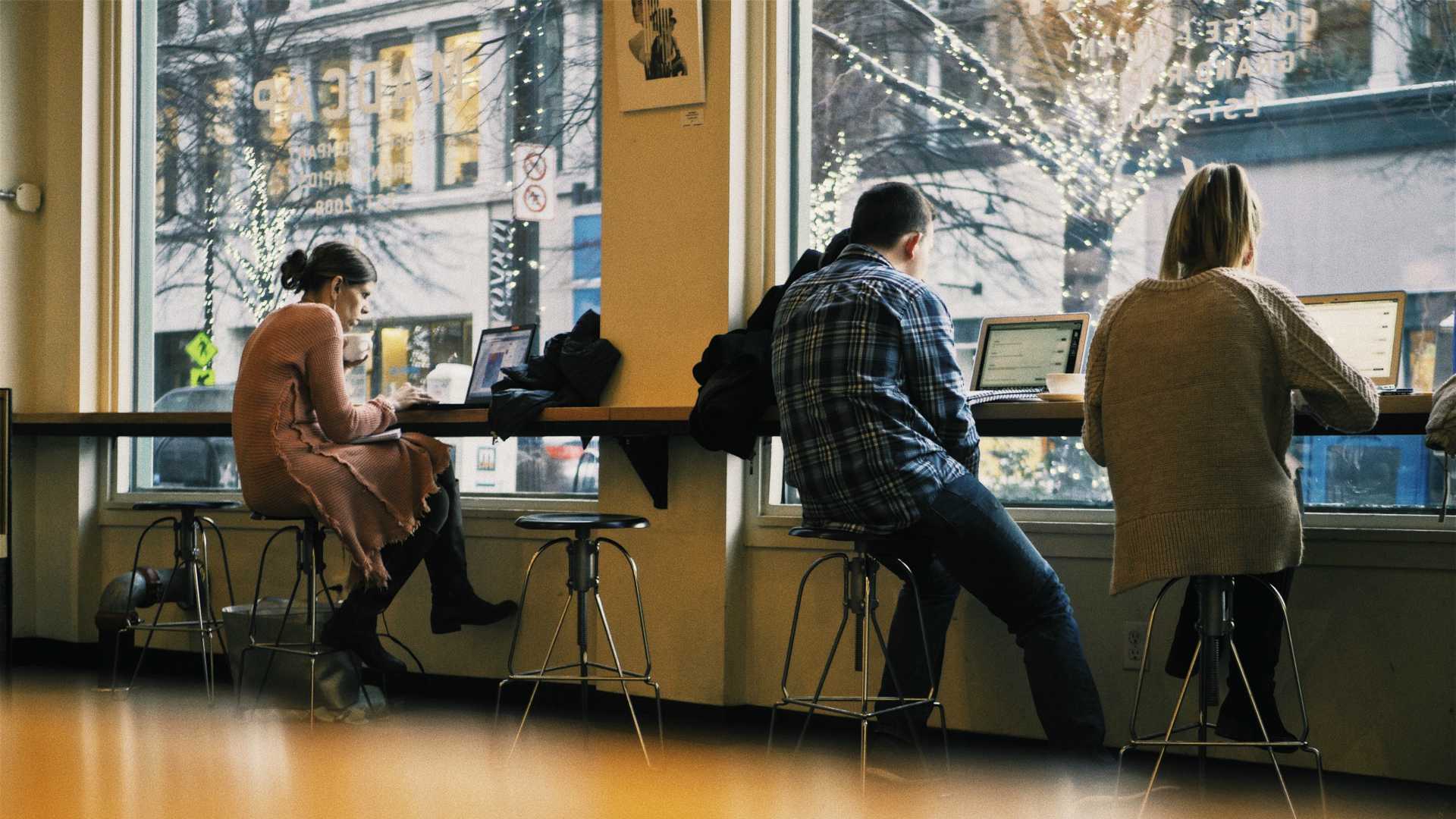 Young remote workers in a coffee shop sitting at the window and working on their laptops