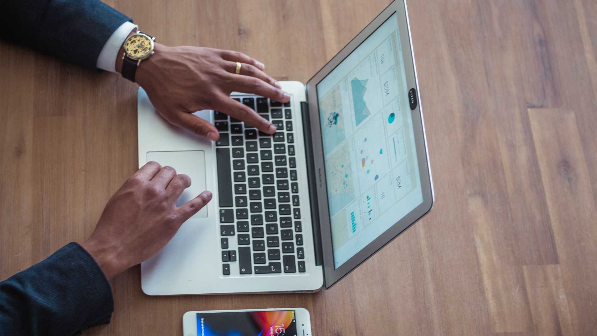 Aerial shot of businessman working on laptop at wooden desk with smartphone next to him