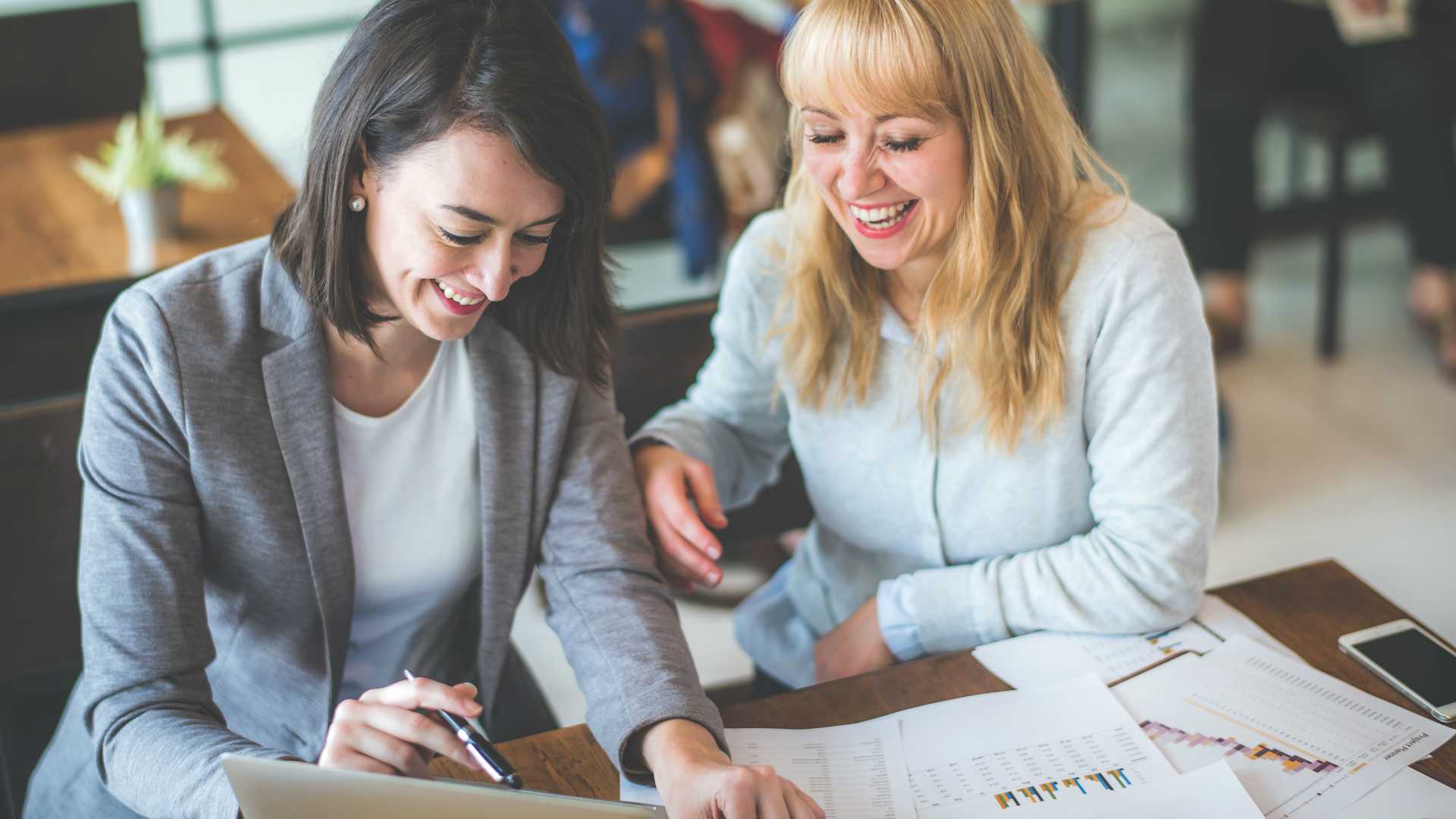 Two female colleagues laughing and working together at wooden desk