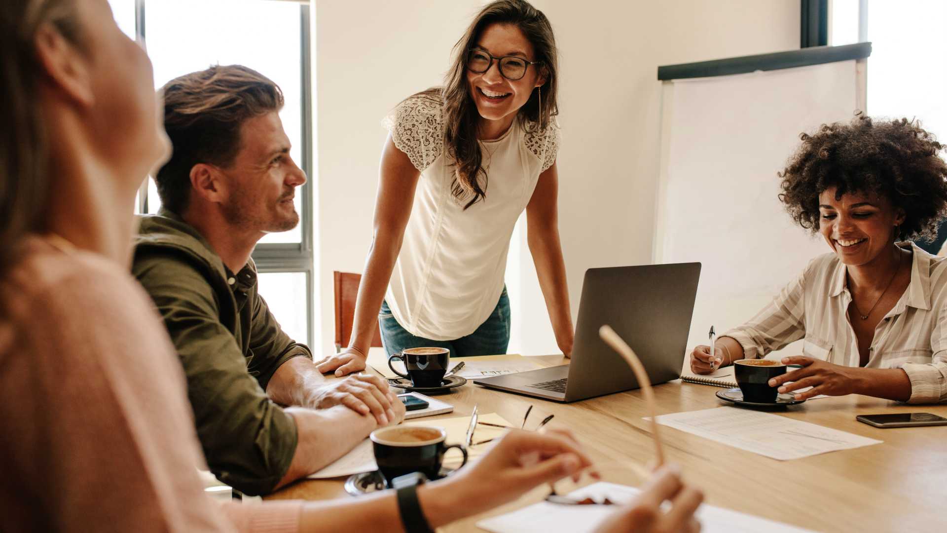 Young, female nonprofit leader smiling and chatting with employees around wooden conference table