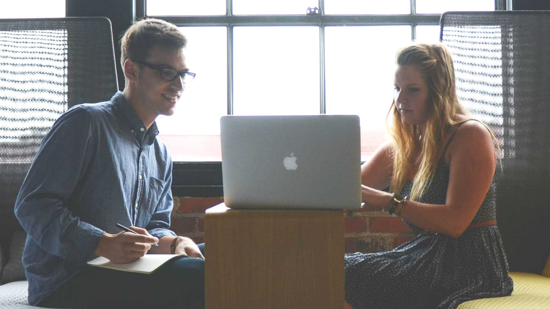 Young businssman and young businesswoman sitting across from each other and providing feedback on each others work