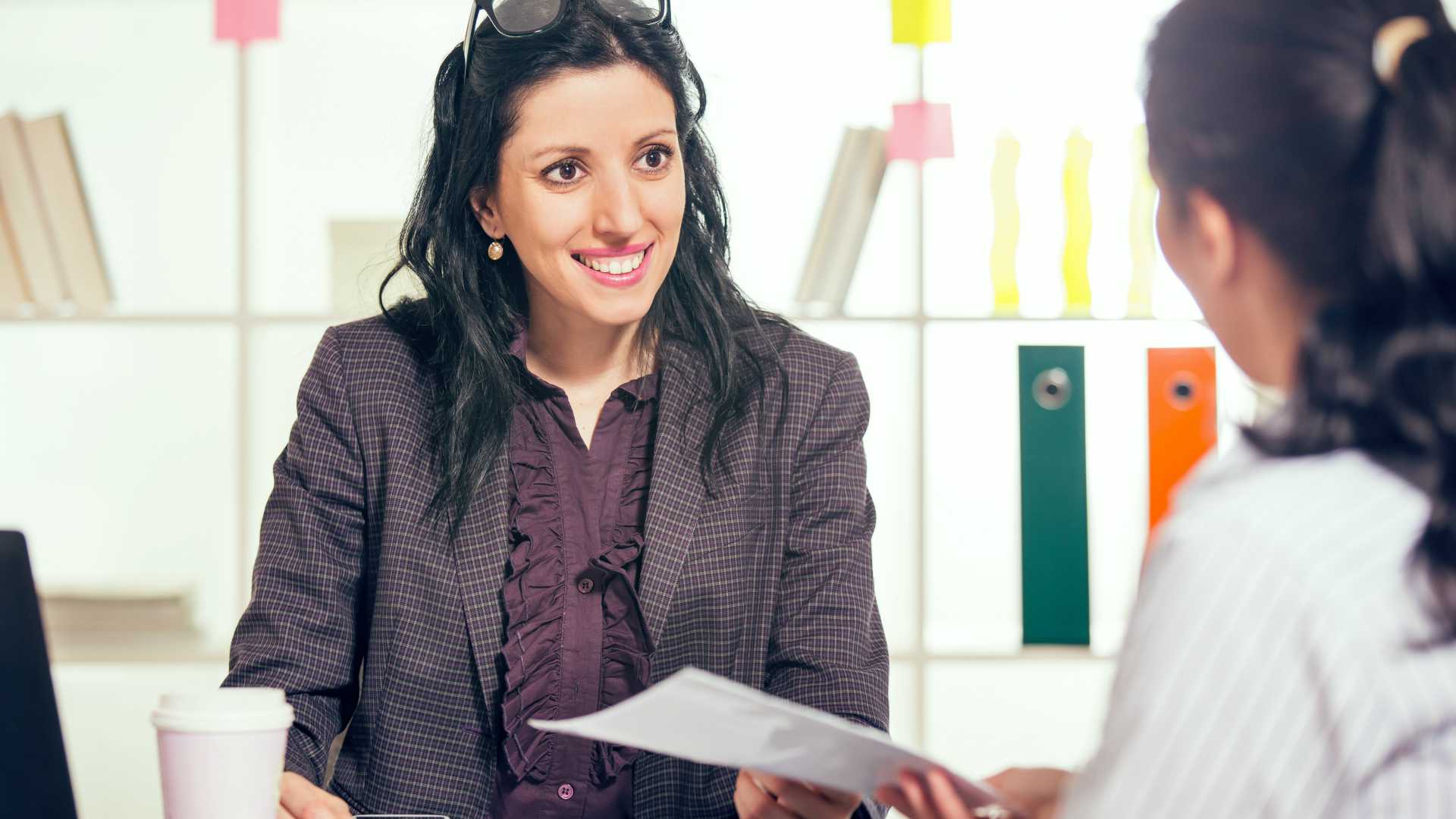 Businesswoman smiling and receiving coaching from female sales manager in brightly lit office