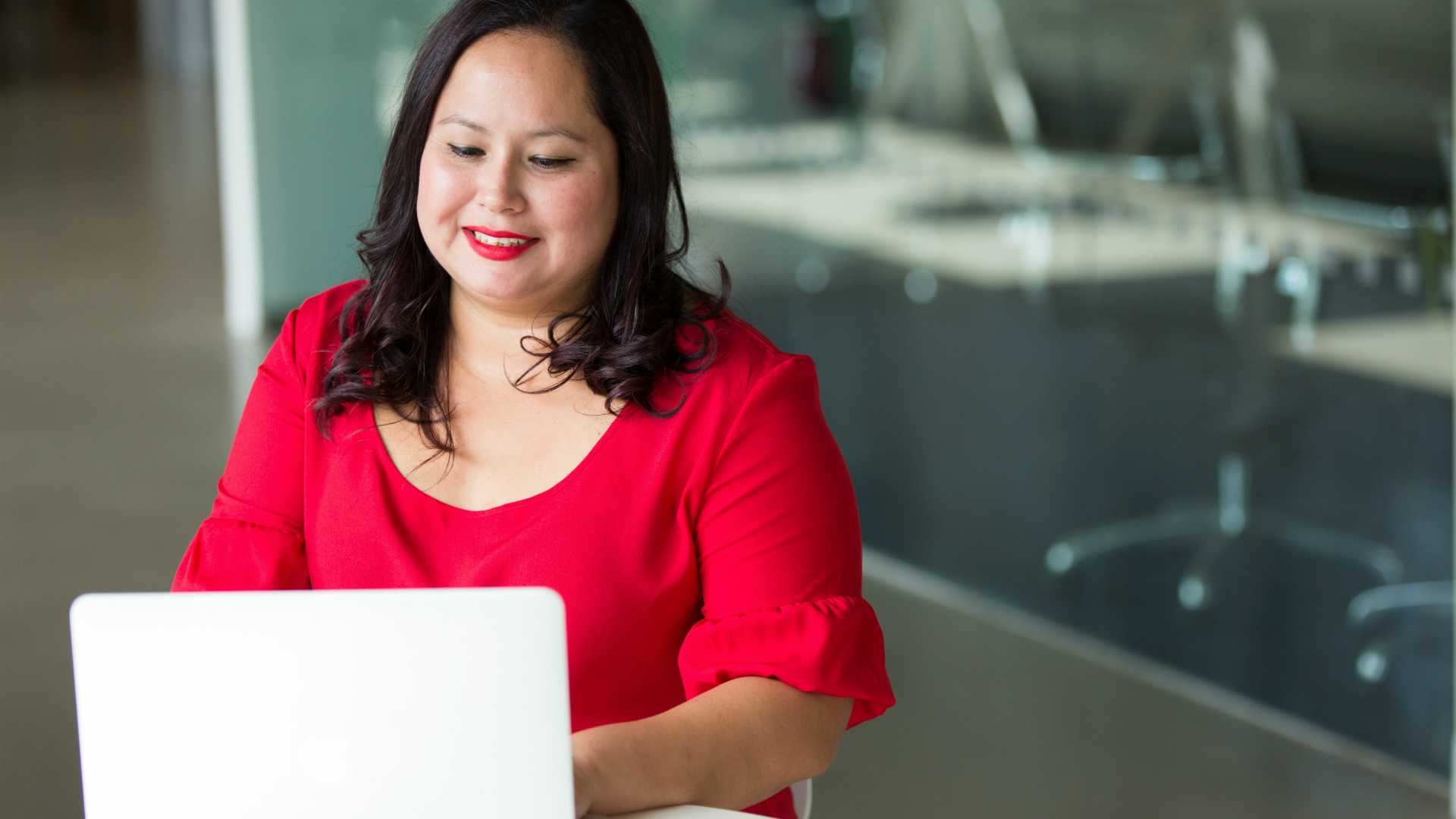 Businesswoman in bright red blouse working at computer in modern officespace