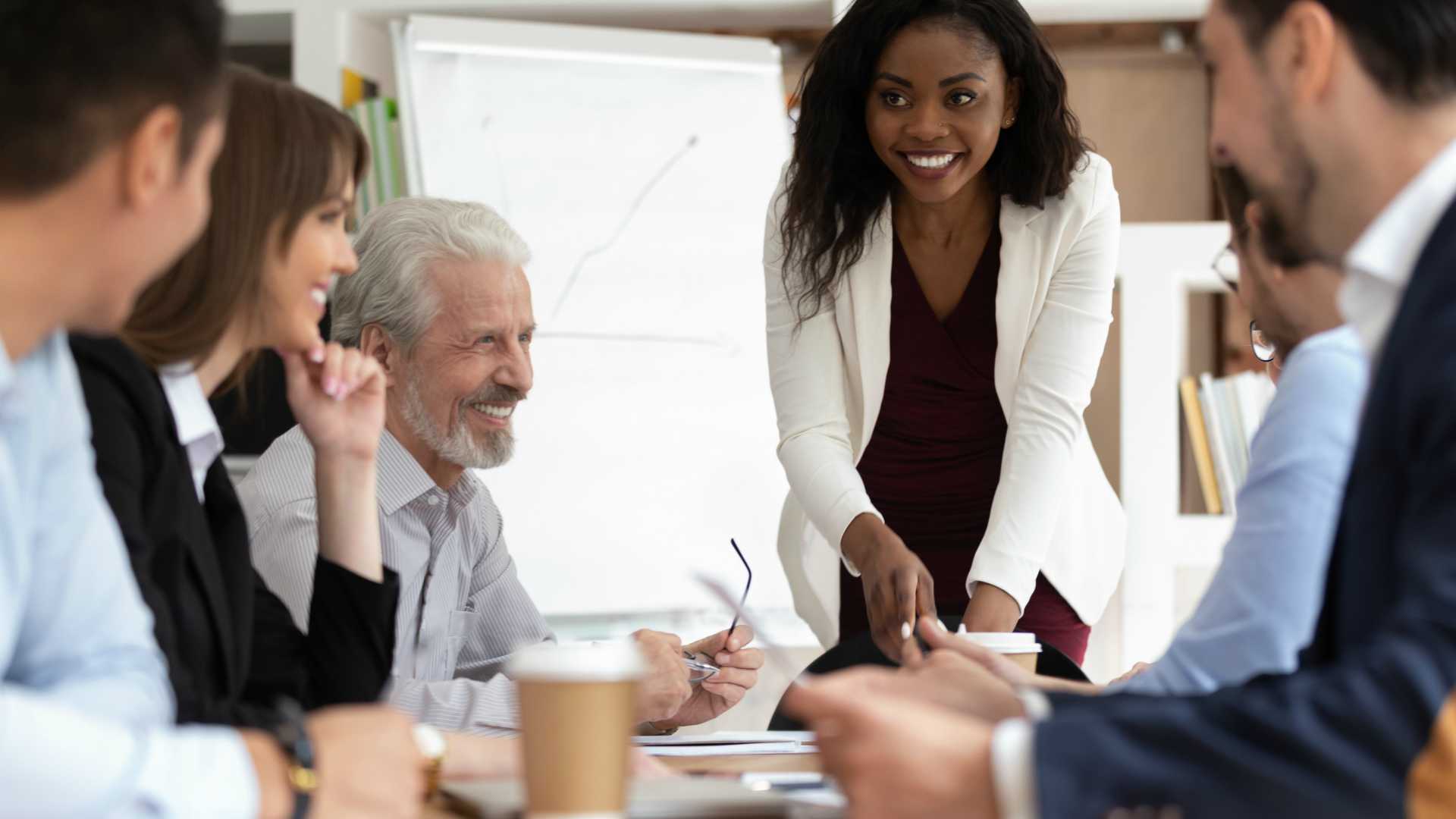 Diverse salesteam smiling and laughing around conference table, discussing sales performance