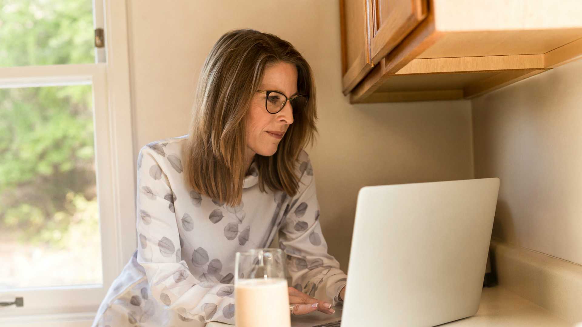 Businesswoman sitting at kitchen counter and participating in webinar on laptop