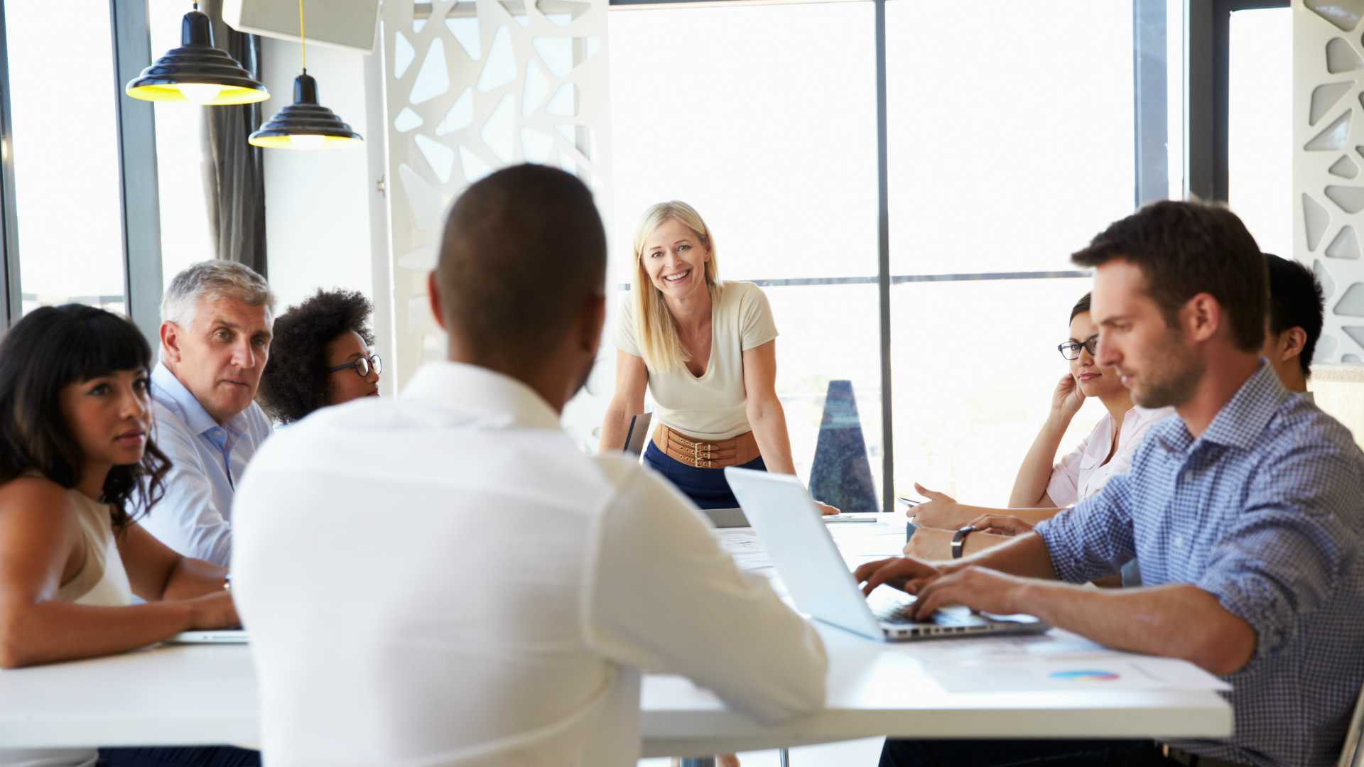 Board room meeting among diverse workforce. Young, blonde businesswoman smiling and laughing at end of the table