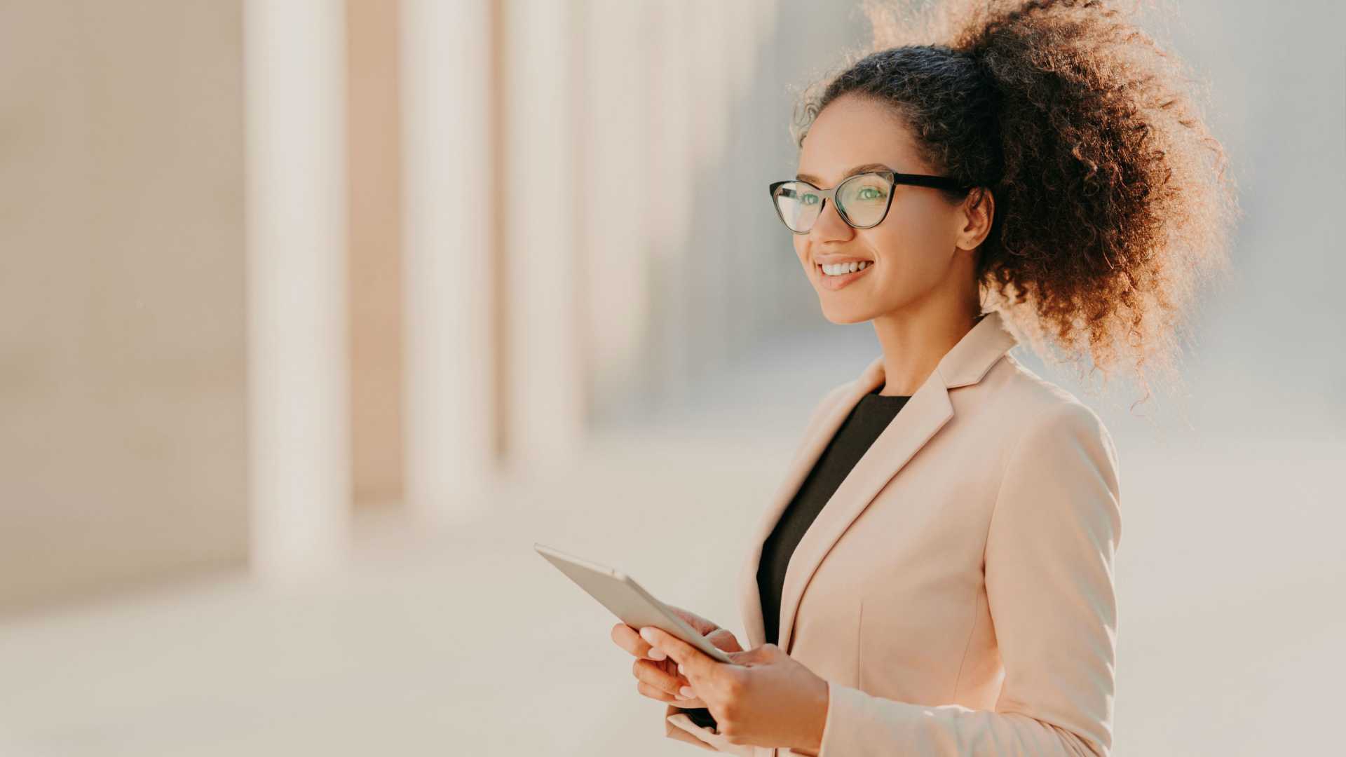 Young, curly-haired business woman smiling confidently and holding tablet
