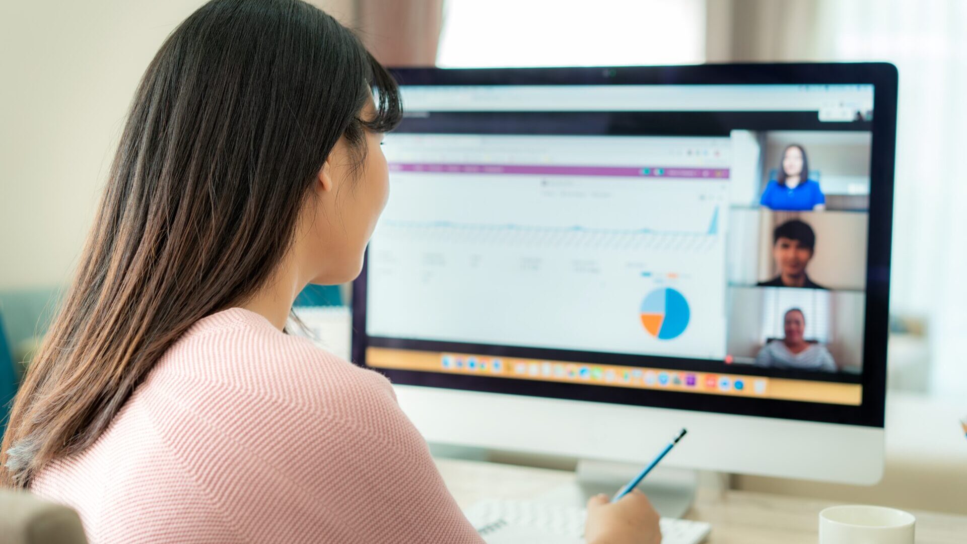 Back view of brunette business woman talking to her colleagues about plan in video conference. Multiethnic business team using computer for a online meeting in video call. Group of people smart working from home.