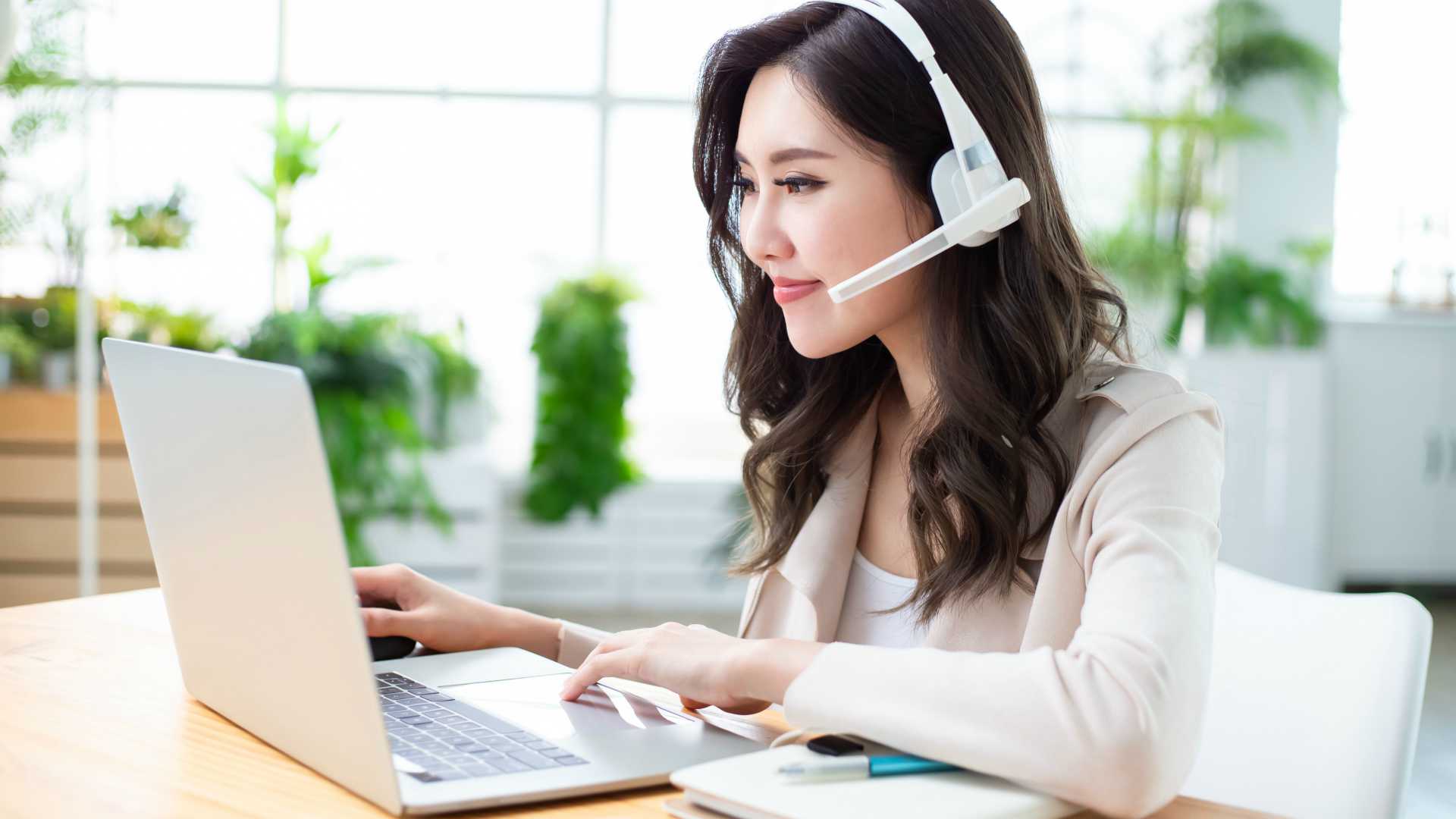 Asian woman using computer and headphone microphone to join a video meeting at home