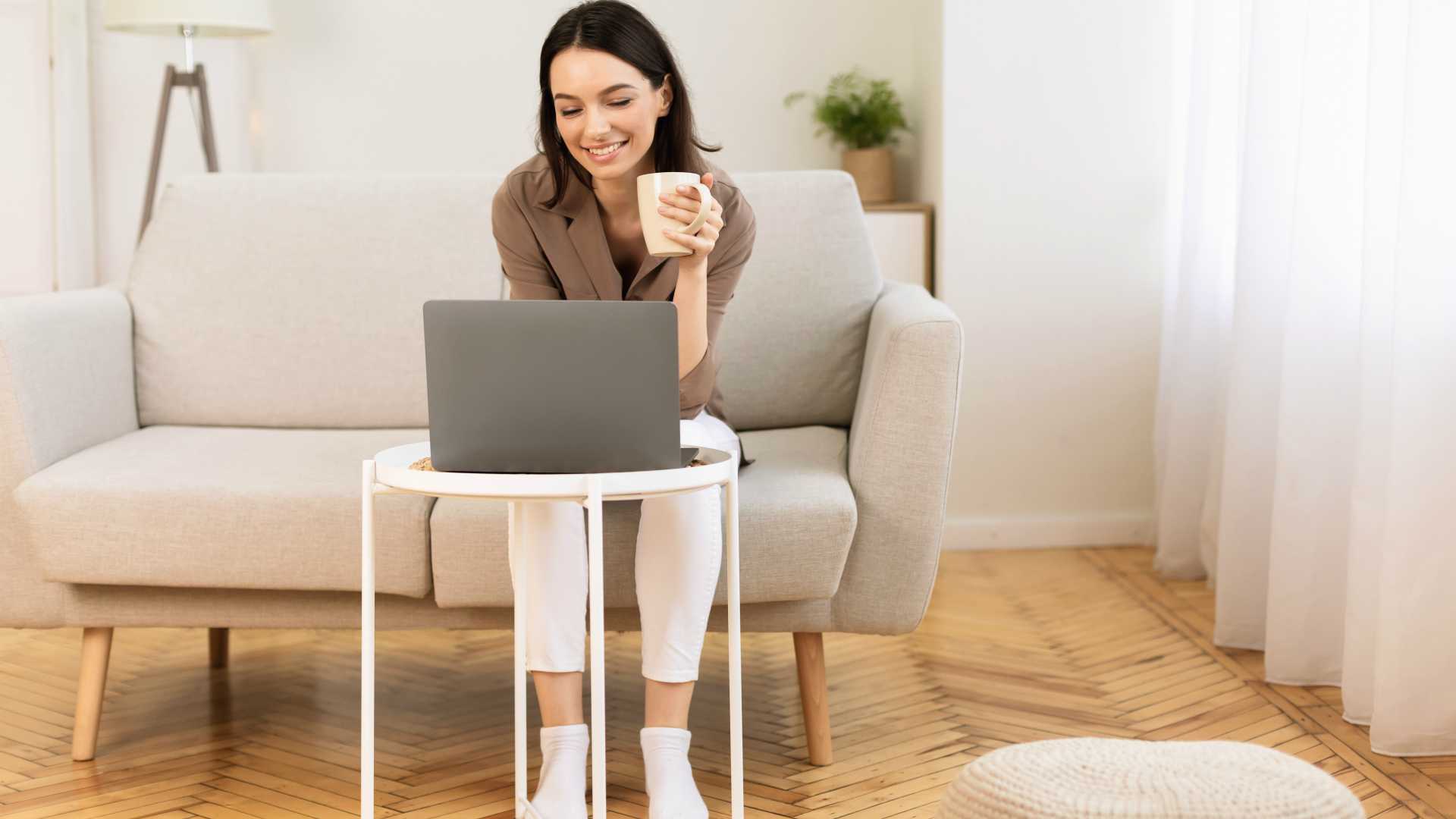 Young businesswoman holding cup of coffee and taking virtual course on laptop
