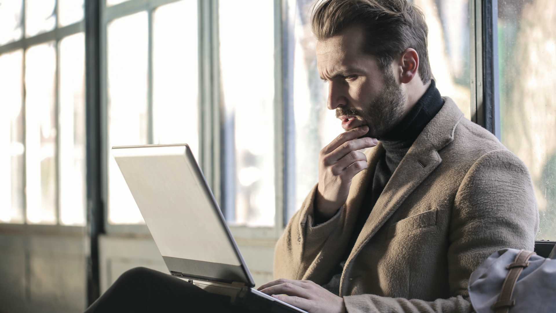 Handsome, beared businessman scratching chin and reading email on laptop