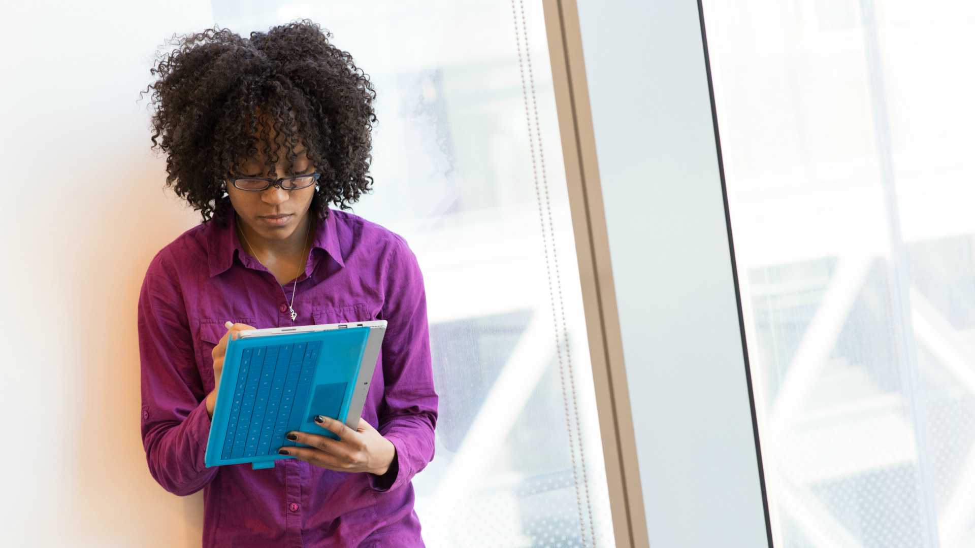 Businesswoman standing inhallway next to window jotting notes in blue notebook