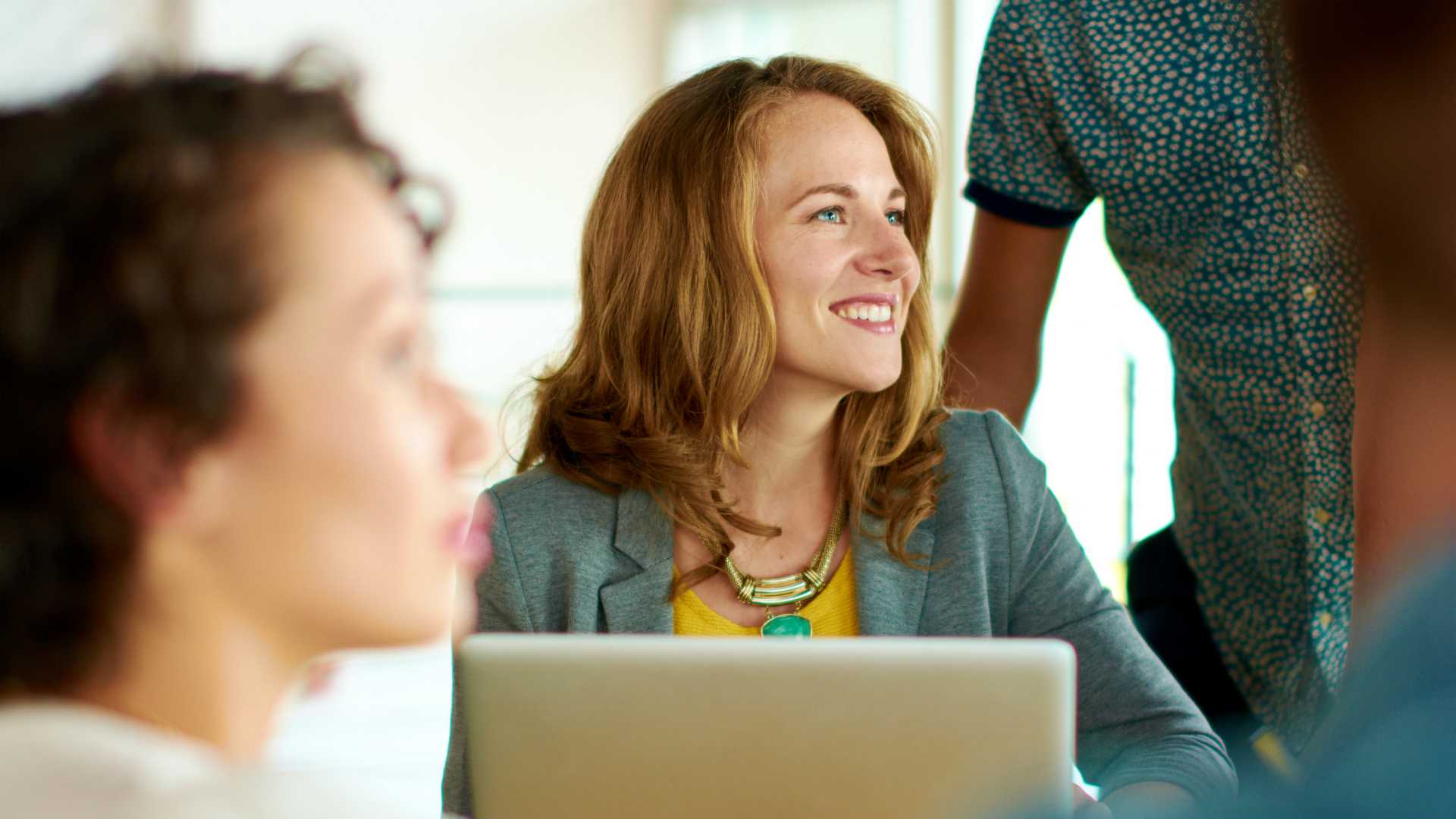 Group of young casual employees discussing a project while researching ideas in a digital touchscreen device and a laptop.