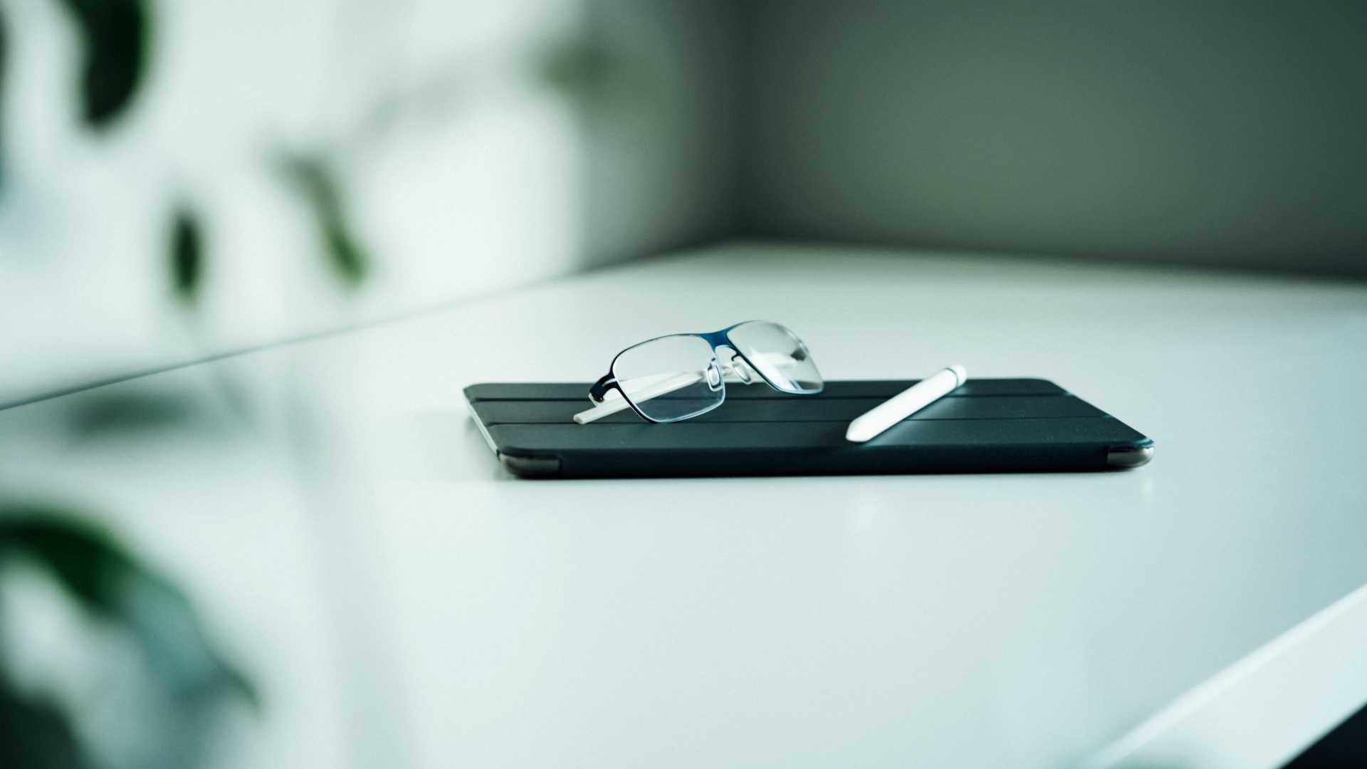Shot focused on eyeglasses sitting on tablet next to stylus