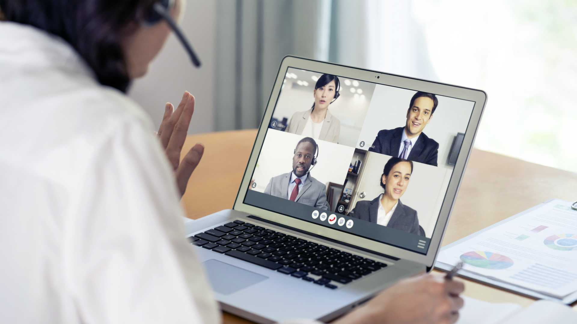 Businesswoman greeting leadership team over video conference call platform, over the shoulder view
