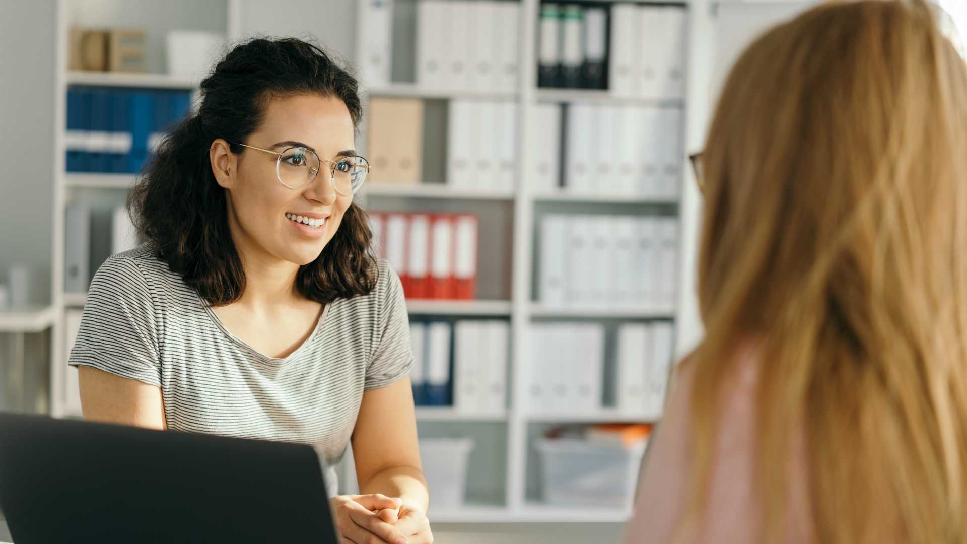 Young woman sitting listening to a business colleague during a meeting in the office in an over the shoulder view