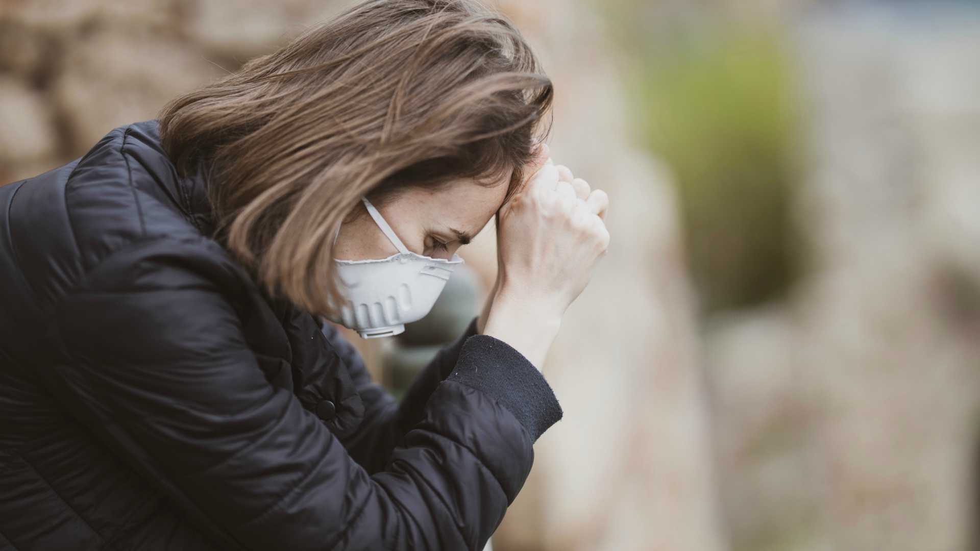 Woman wearing face mask and holding head on hands sitting outside